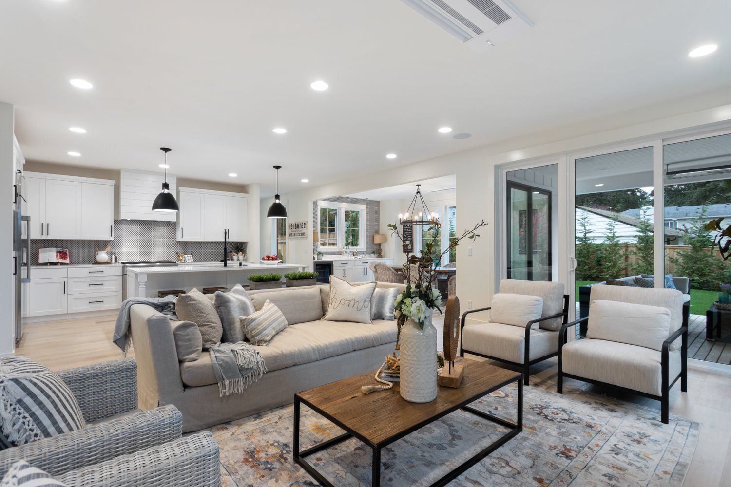 Open-concept living space with kitchen, living area, and sliding door to backyard. Neutral colors and modern furniture.