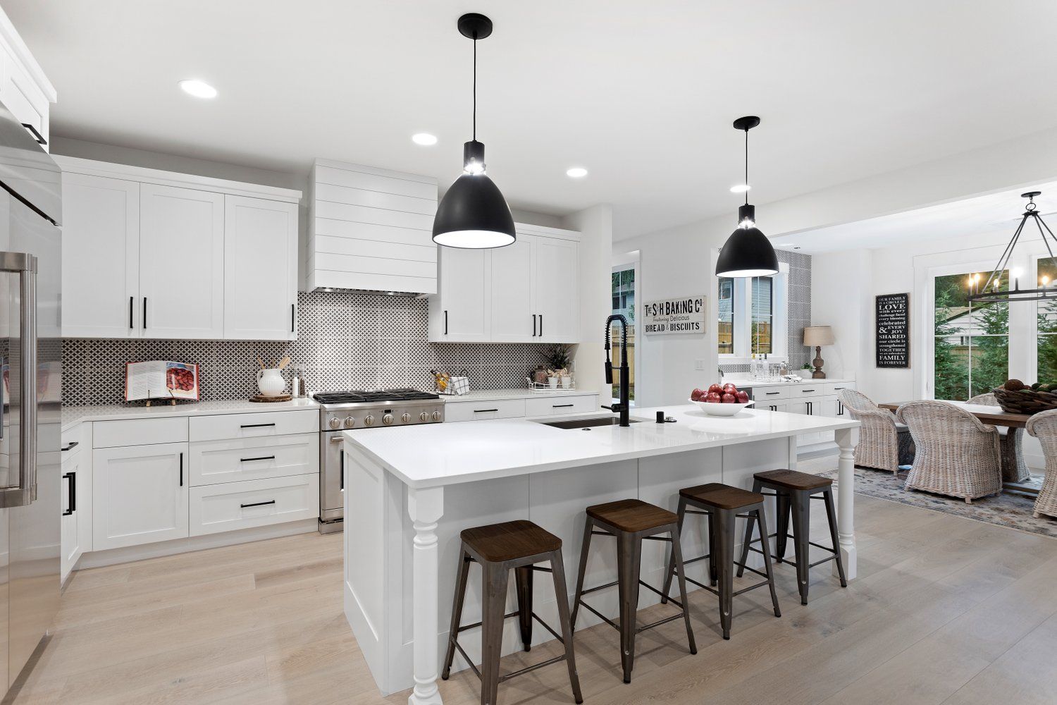 Modern white kitchen with an island, black pendant lights, and wooden bar stools.