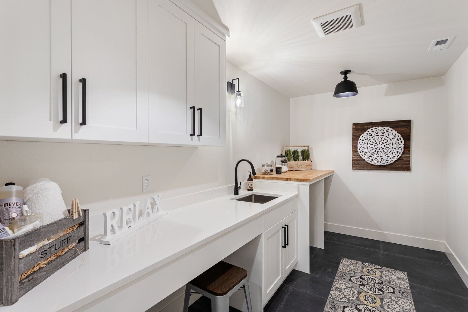 White laundry room with cabinets, sink, black accents, and a rug on the floor.