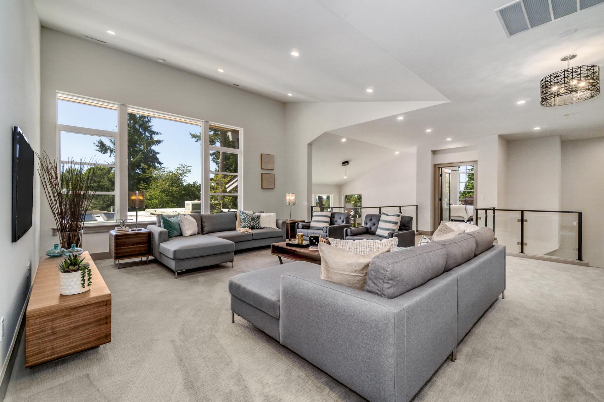 Spacious living room with grey sofas, large windows, and light-colored walls.
