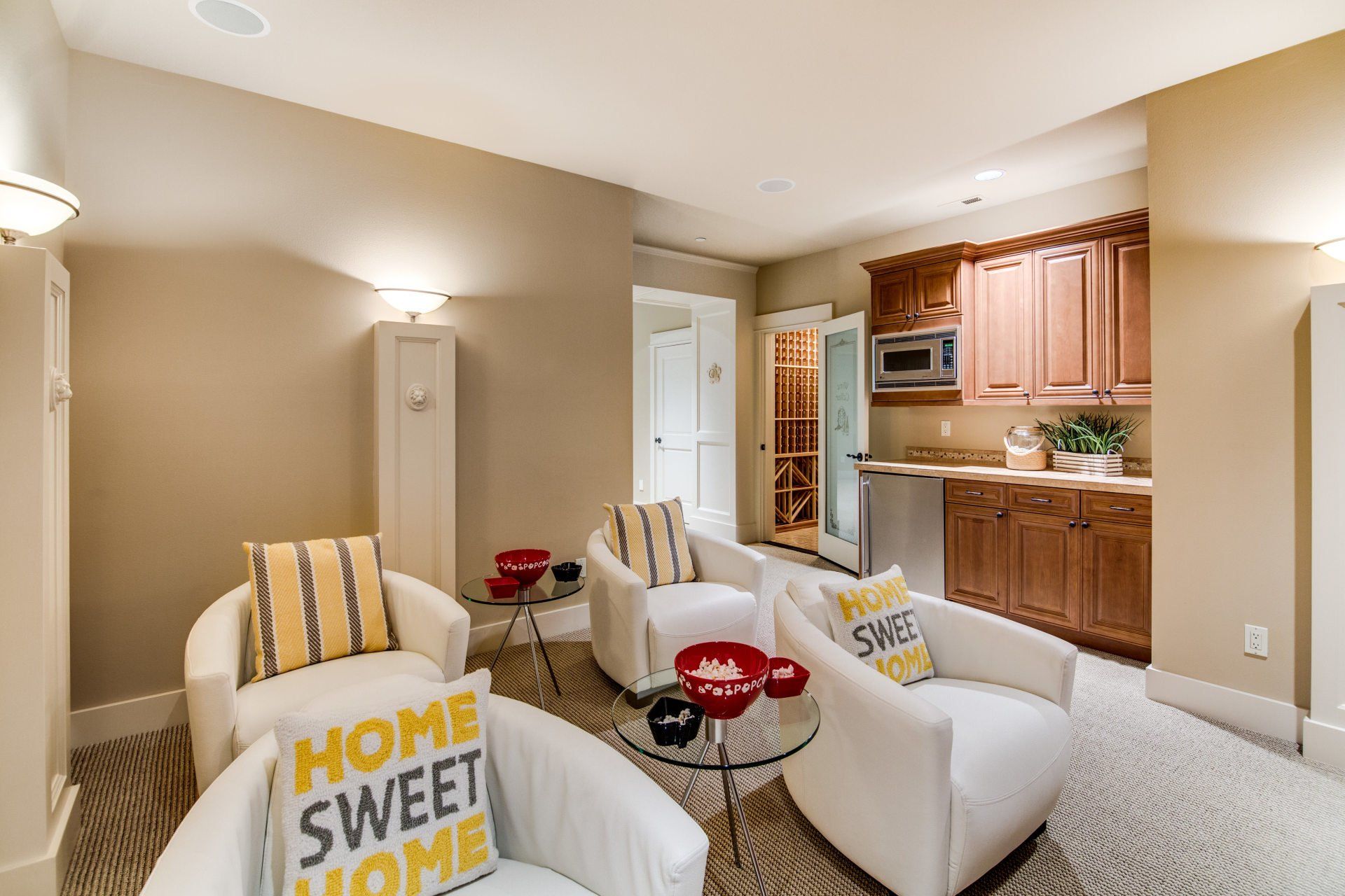 Cozy seating area with white chairs, red side tables, rug, small kitchen with brown cabinets.