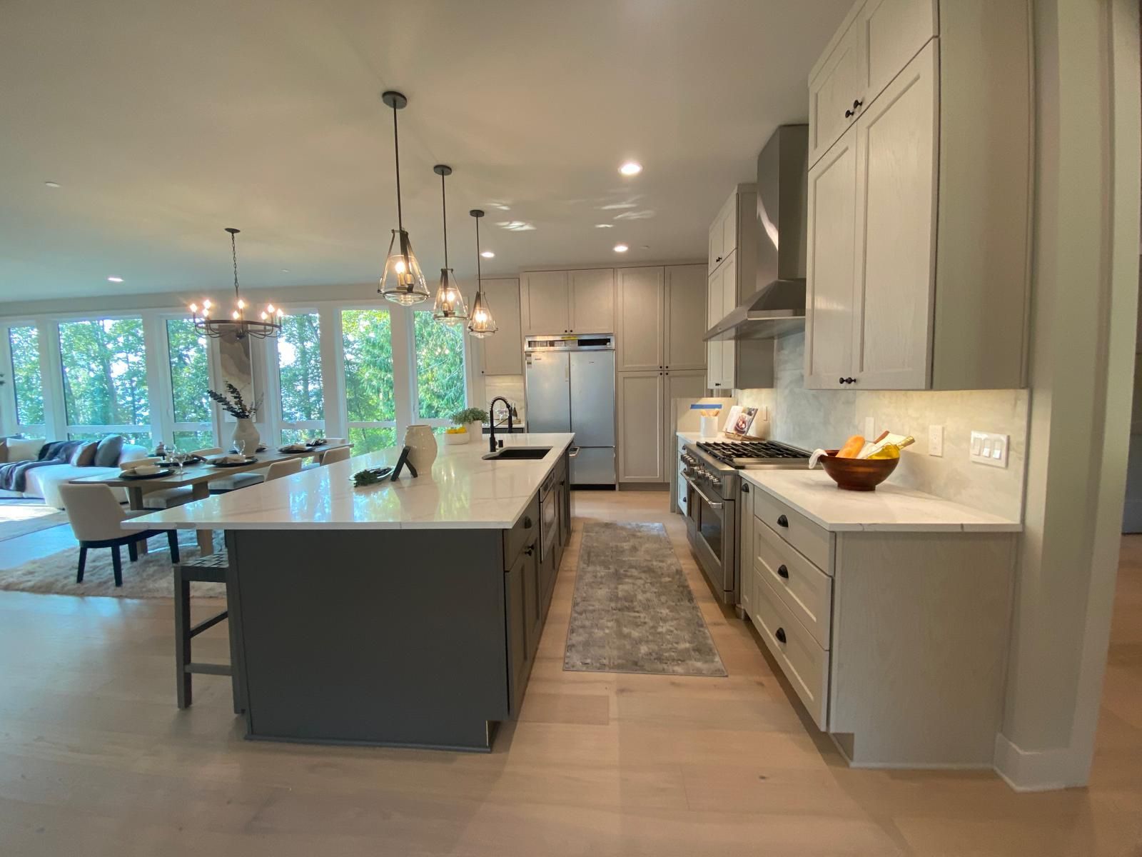 Spacious modern kitchen with island, gray cabinets, stainless steel appliances, and large windows.