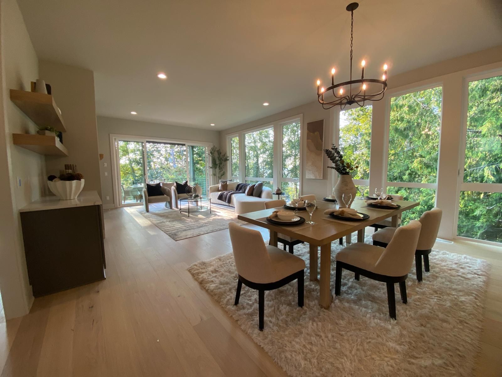 Dining room with table set for six, surrounded by windows with a lush green view.