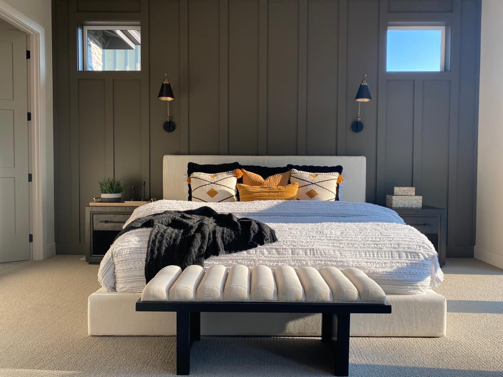 Bedroom with dark accent wall, bed, bench, and two small windows.