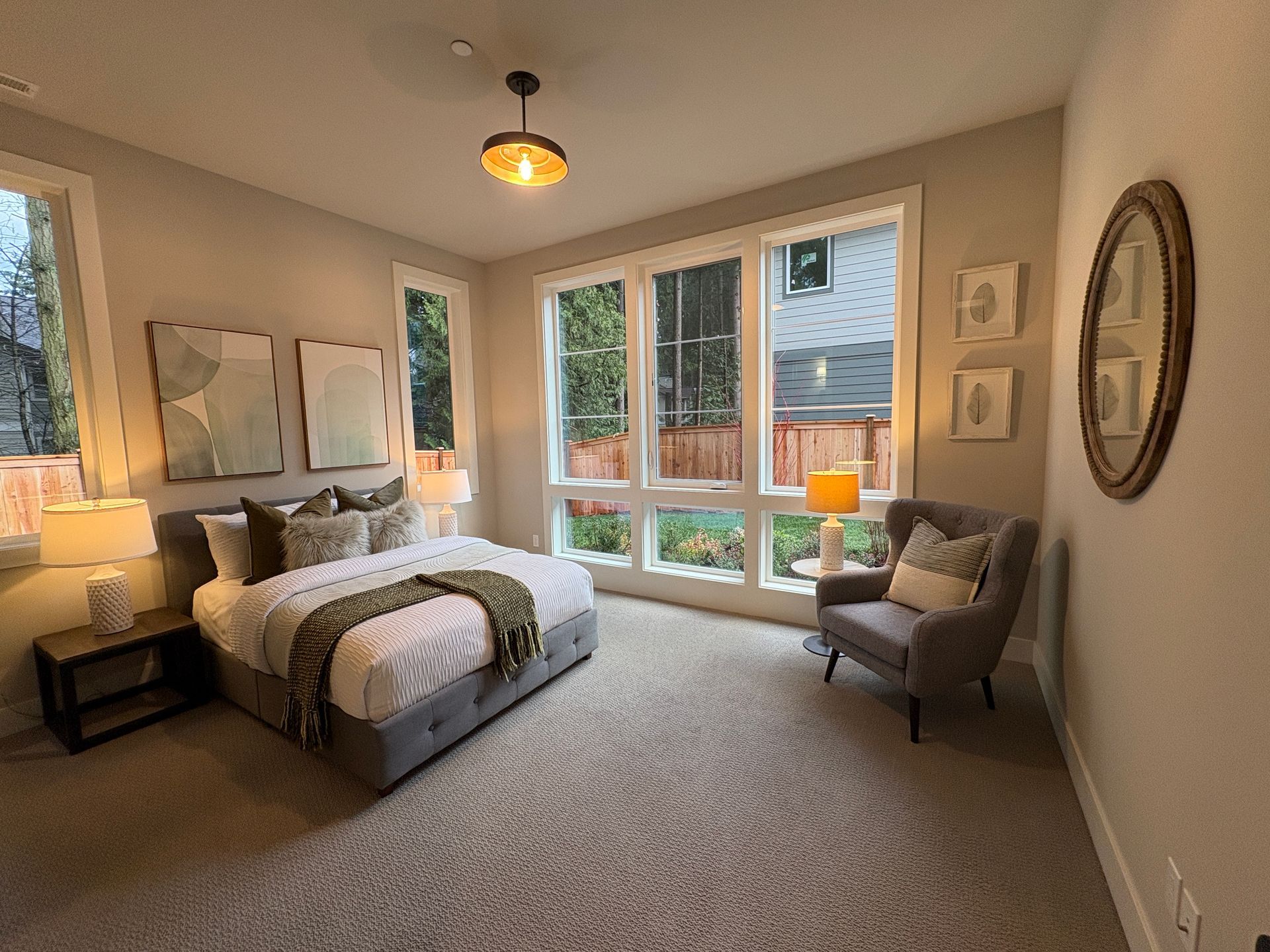 Bedroom with bed, chair, windows, and artwork. Gray and white color scheme. Natural light.