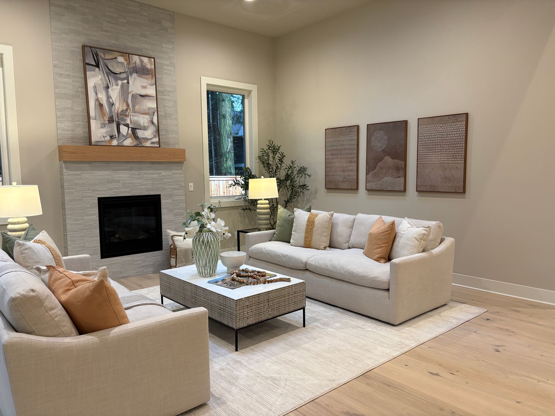 Living room with fireplace, sofas, and art. Beige walls and hardwood floor.