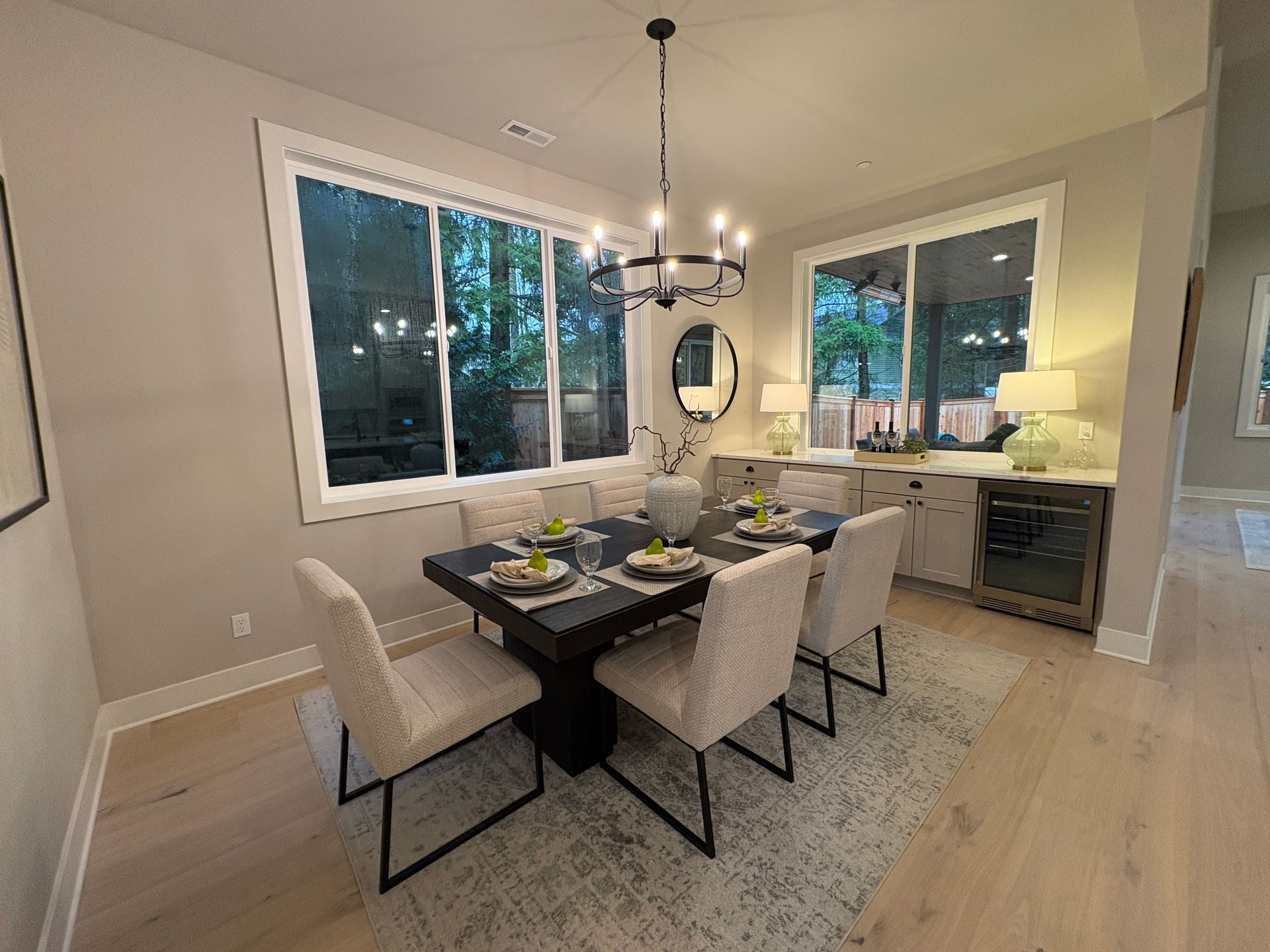 Formal dining room with dark table, six chairs, and chandelier. Large windows with outdoor view.