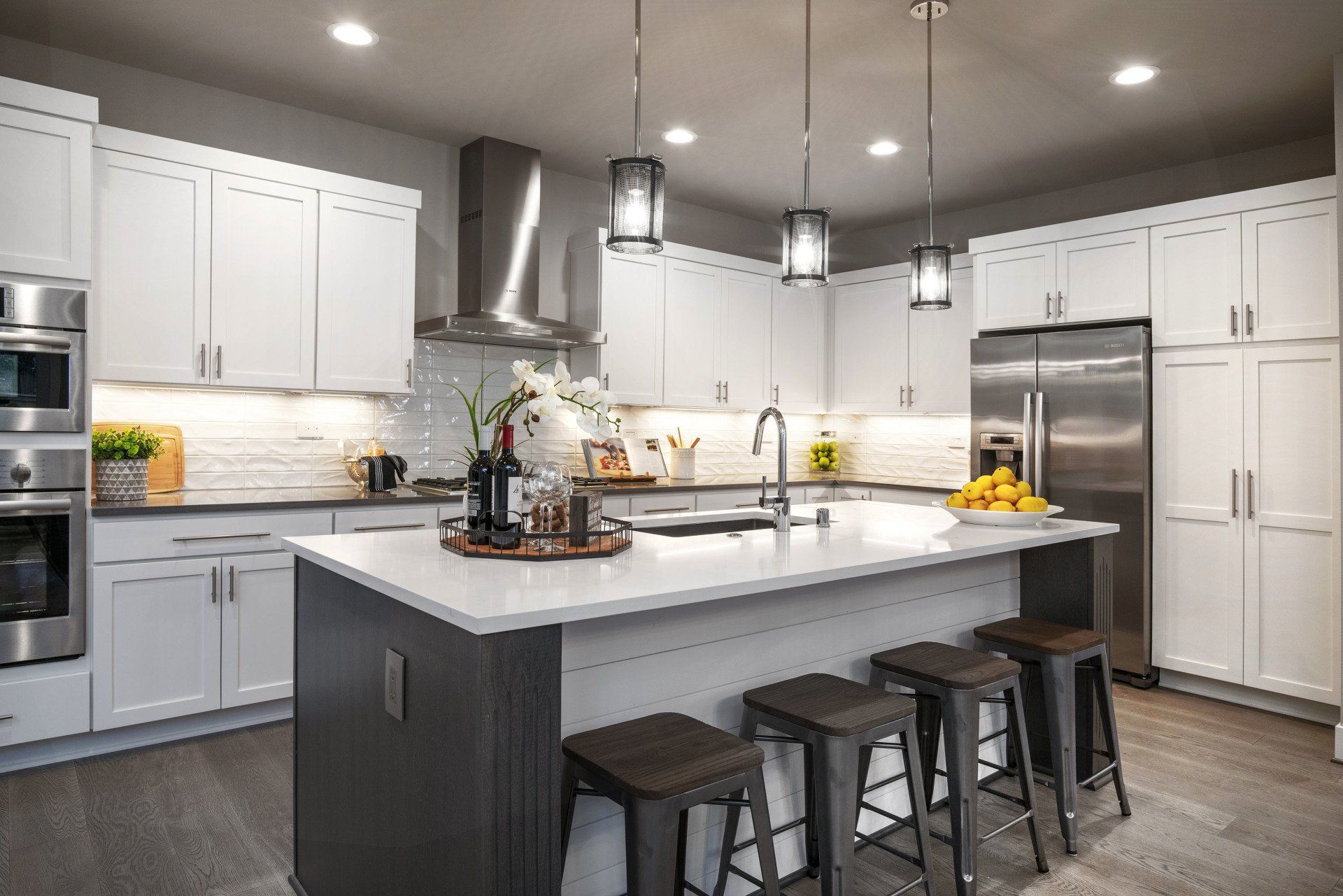 Modern white kitchen with gray island, stainless steel appliances, and stools.