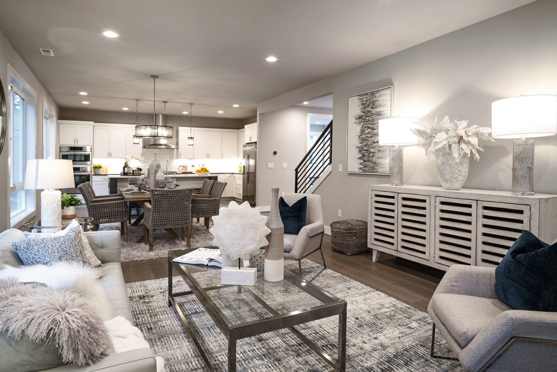 Modern living room with open kitchen, dining area, and gray furniture.