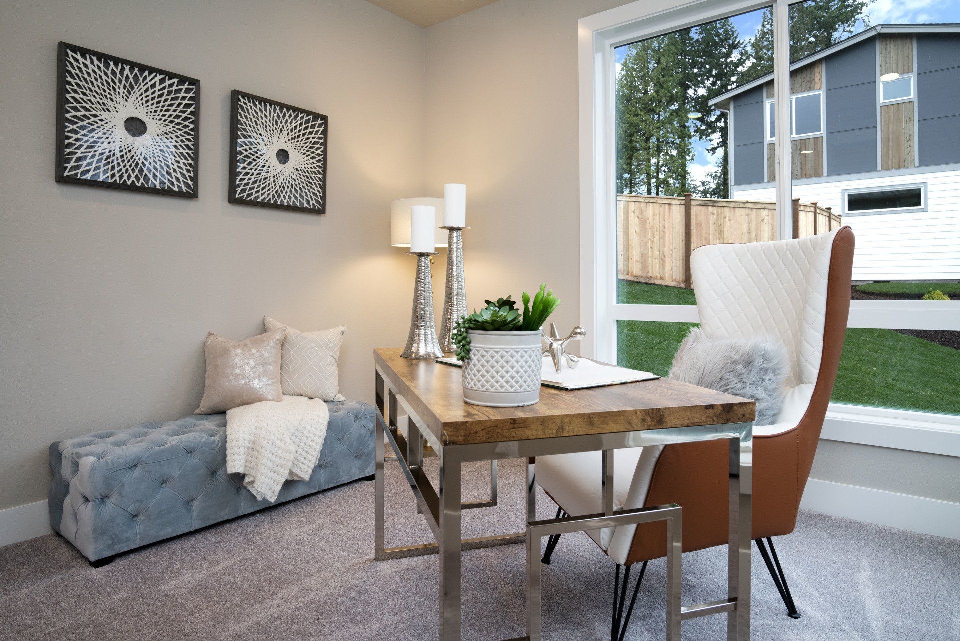 A home office with a desk, chair, and bench near a window overlooking a yard.