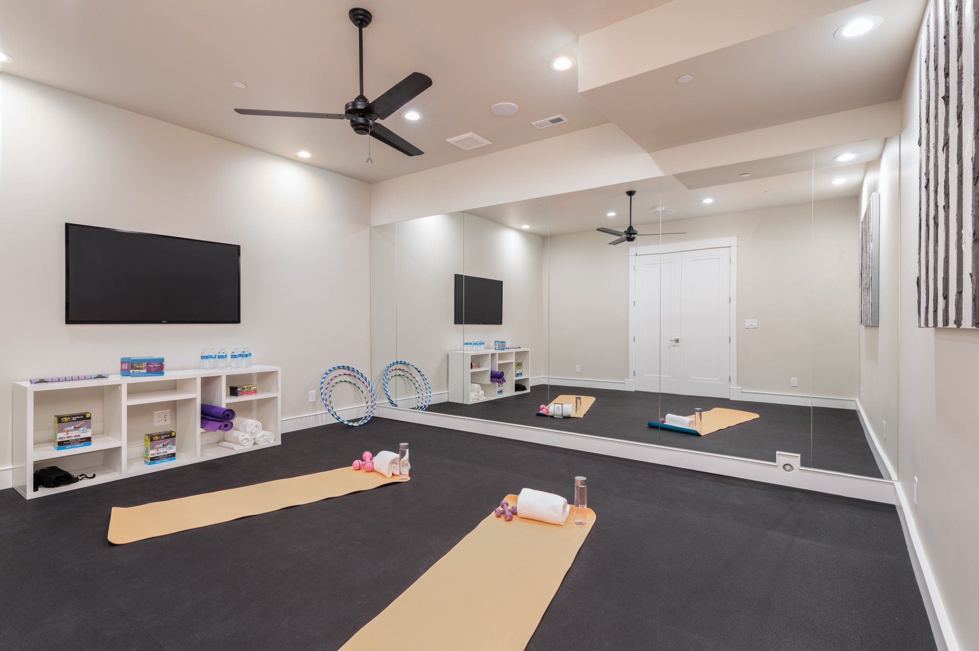 Yoga/exercise room with mats, mirrors, storage, and a TV; black flooring, white walls.