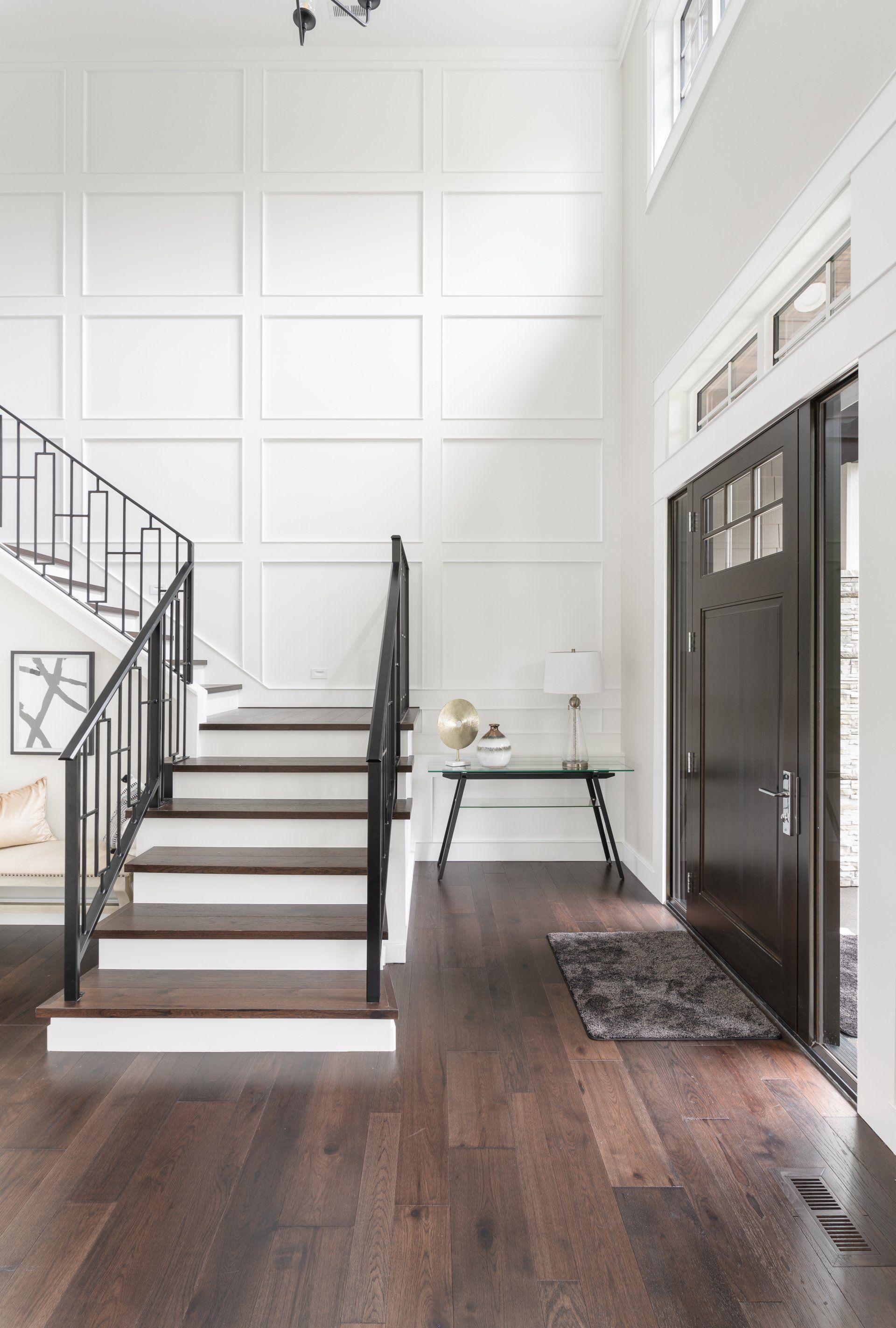 A grand entryway with a dark wood floor, white walls, and a staircase with a black metal railing.
