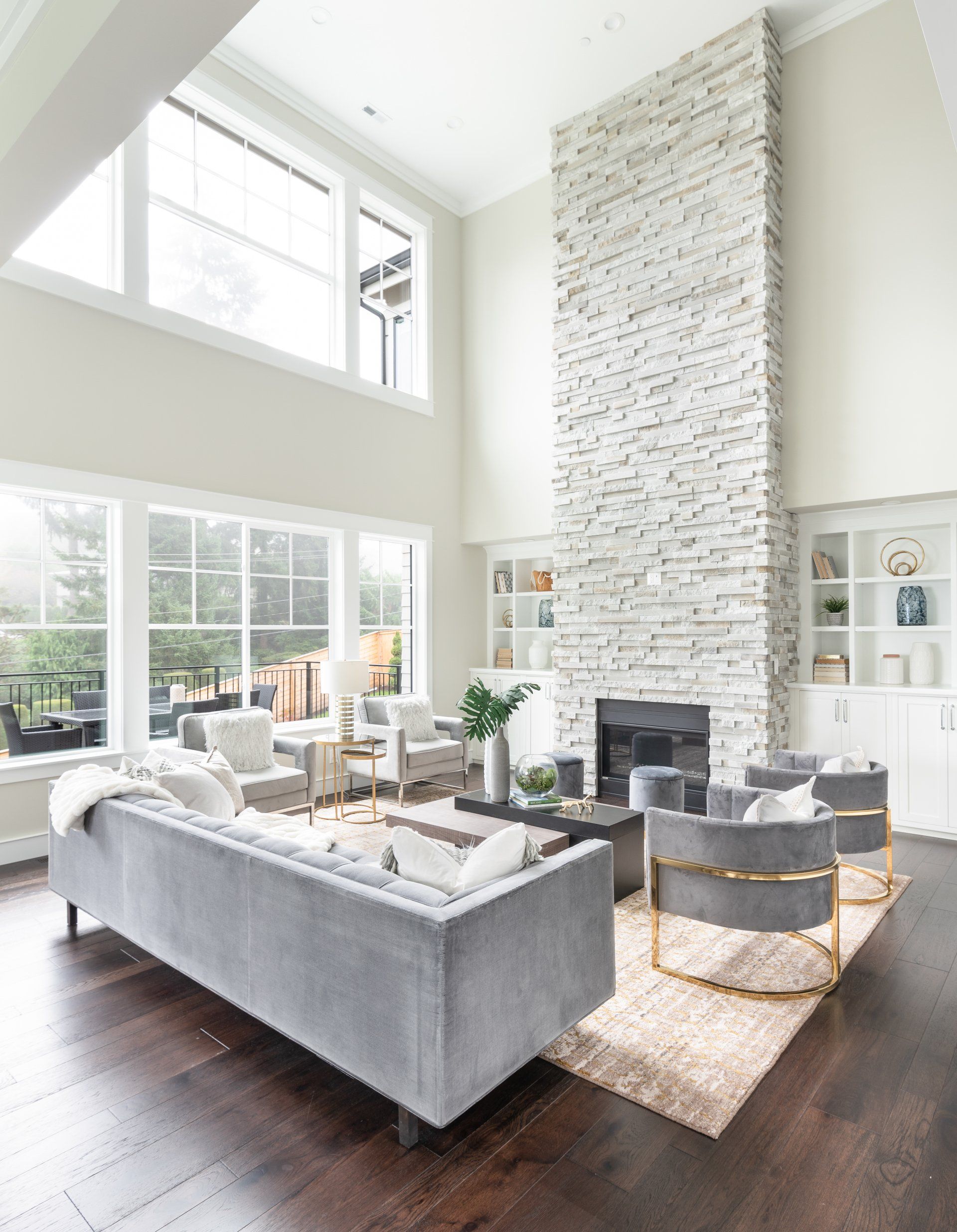 Spacious living room with a stone fireplace, large windows, and gray furniture.