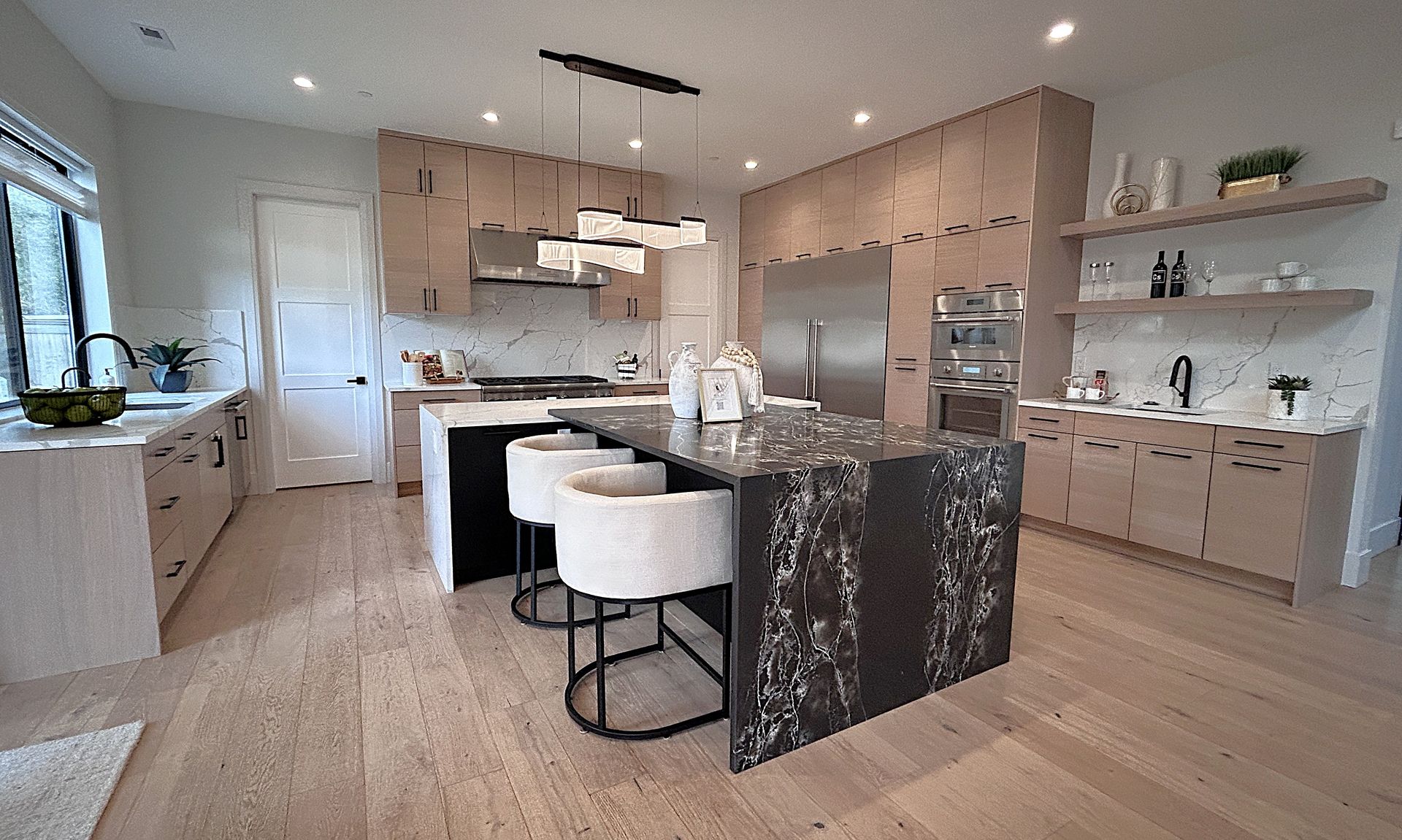 Modern kitchen with island, white bar stools, stainless appliances, and light wood cabinets