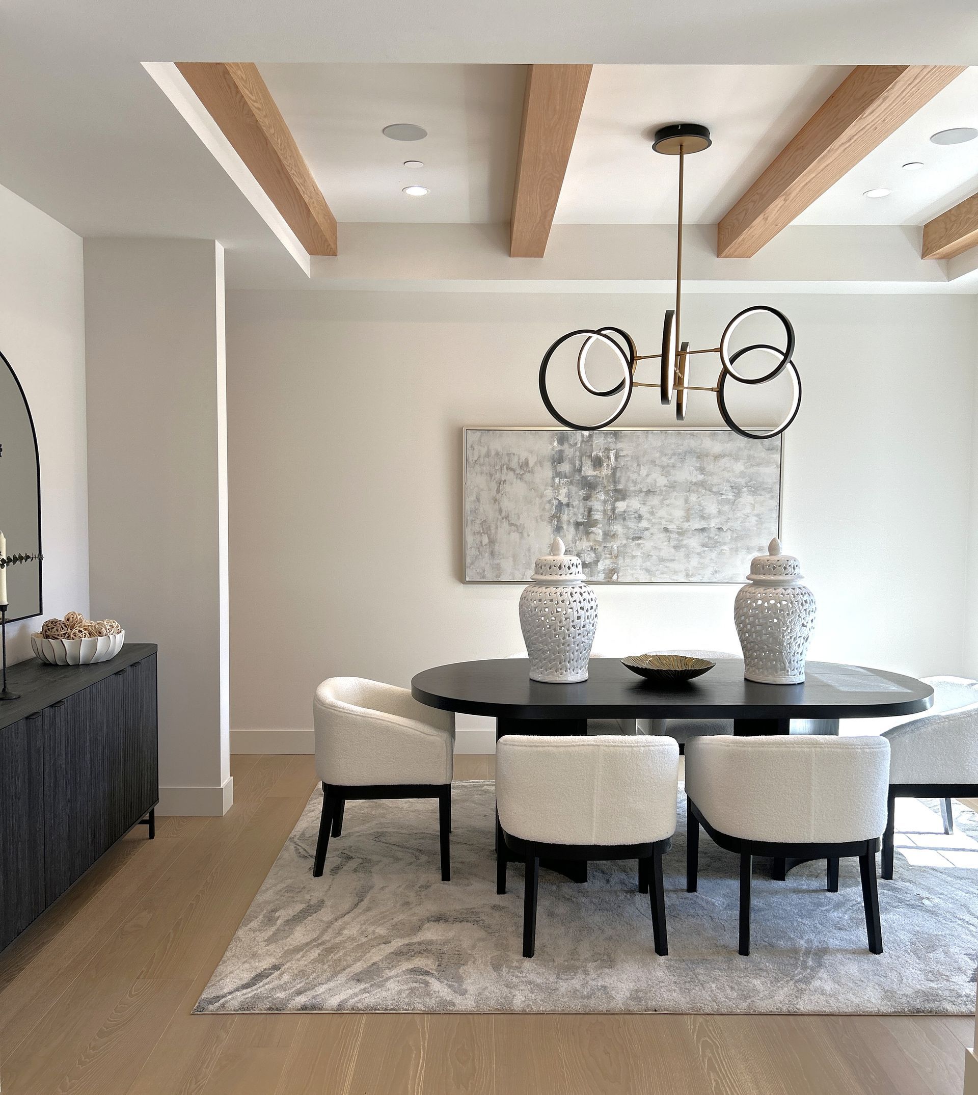 Modern dining room with a round table, upholstered chairs, chandelier, and exposed wood ceiling beams