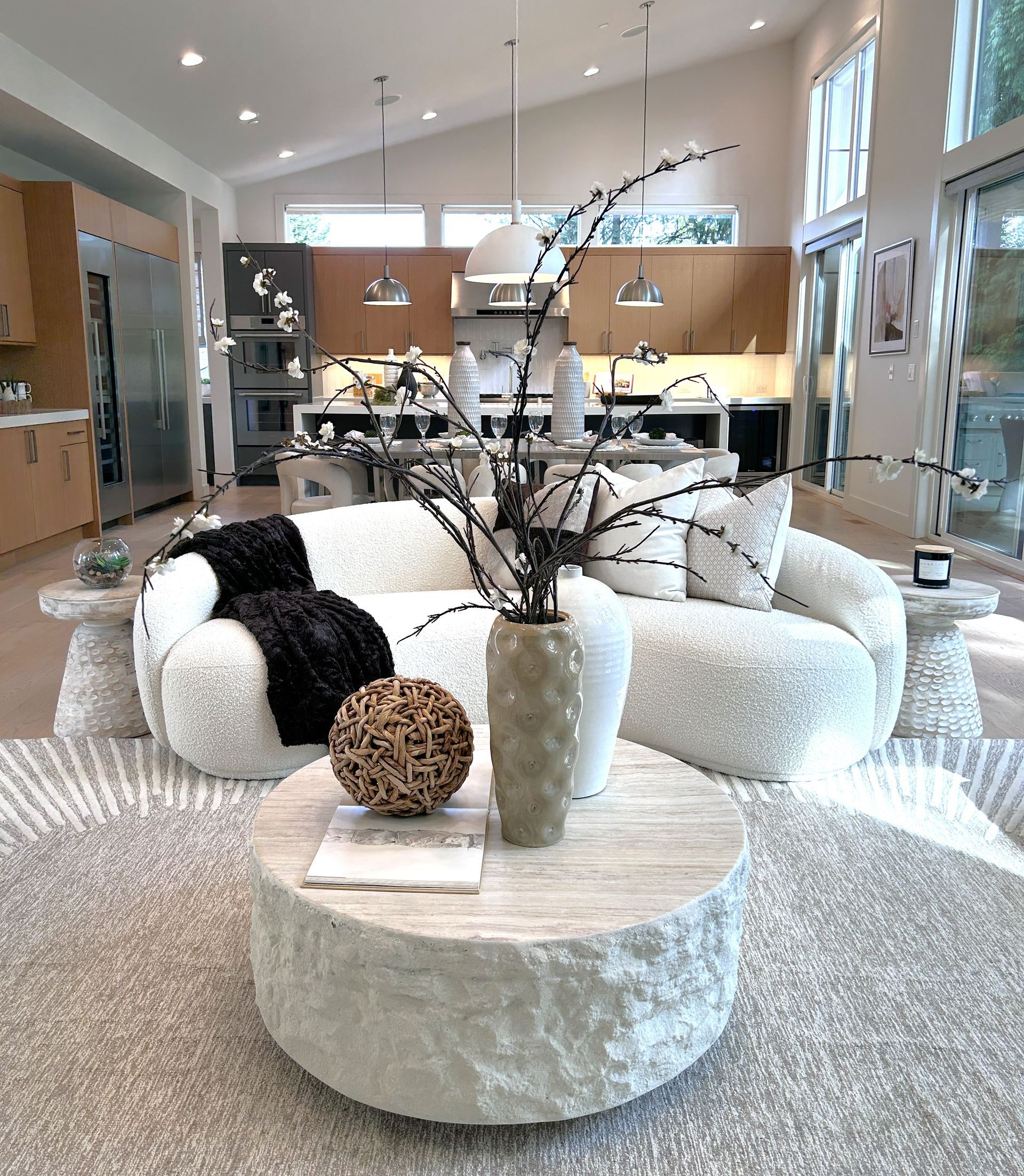 Bright modern living room with white sofas, round stone coffee table, and open kitchen in background