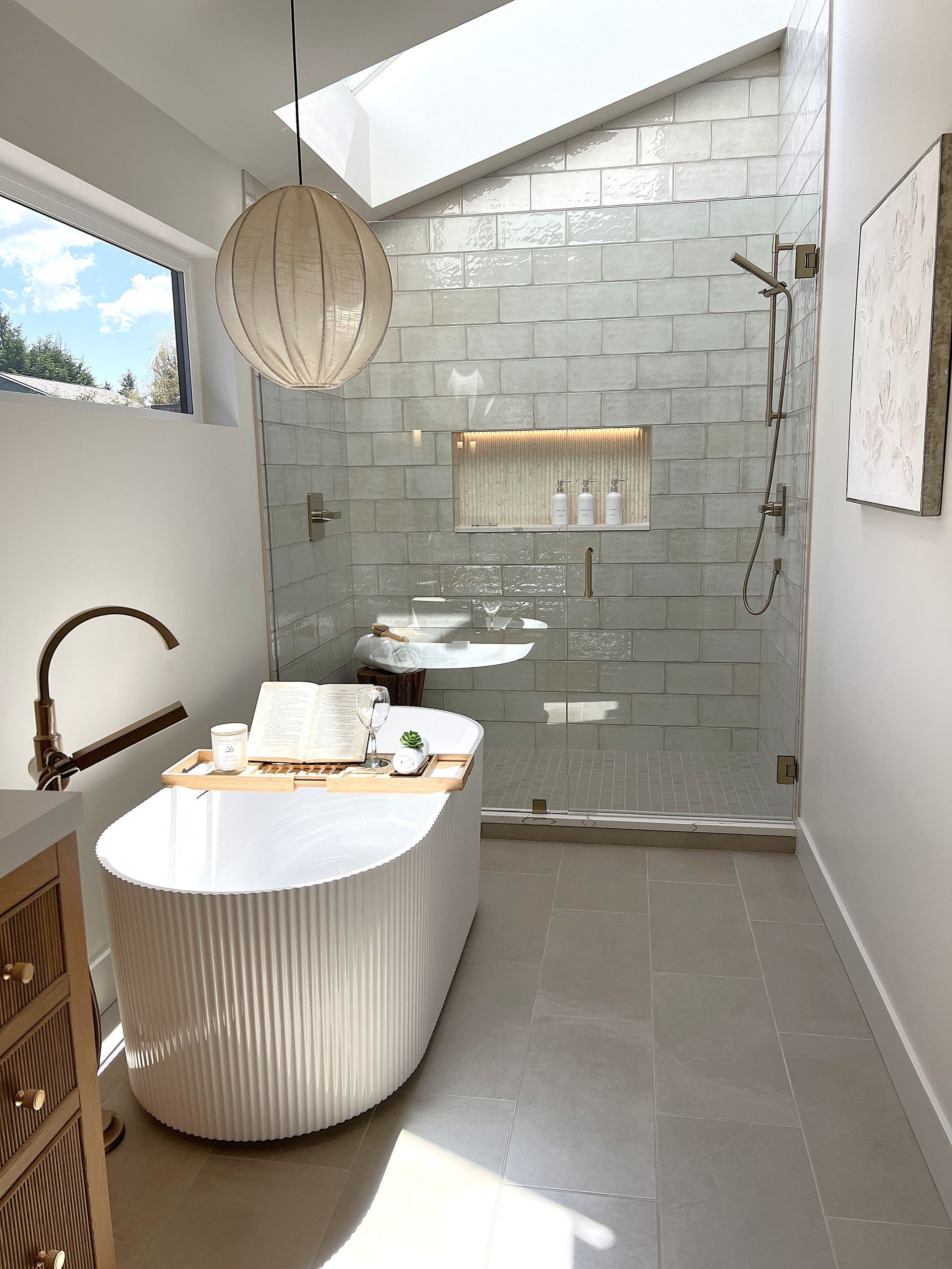 Modern bathroom with freestanding tub, glass shower, and skylight in neutral tones