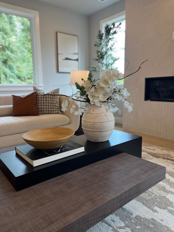 Living room with modern decor: beige sofa, black coffee table with vase of white flowers, and an accent bowl.