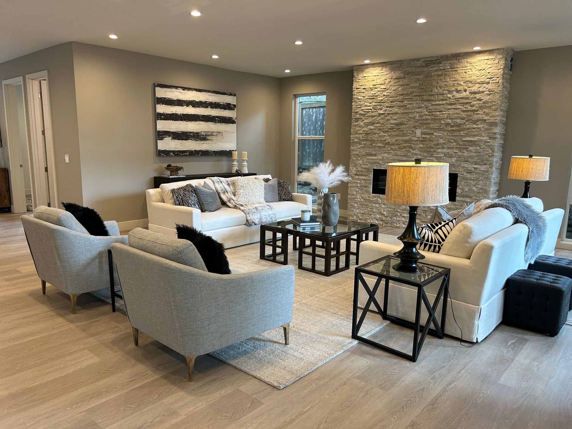 Modern living room with white and gray furniture, stone fireplace, artwork, and area rug.