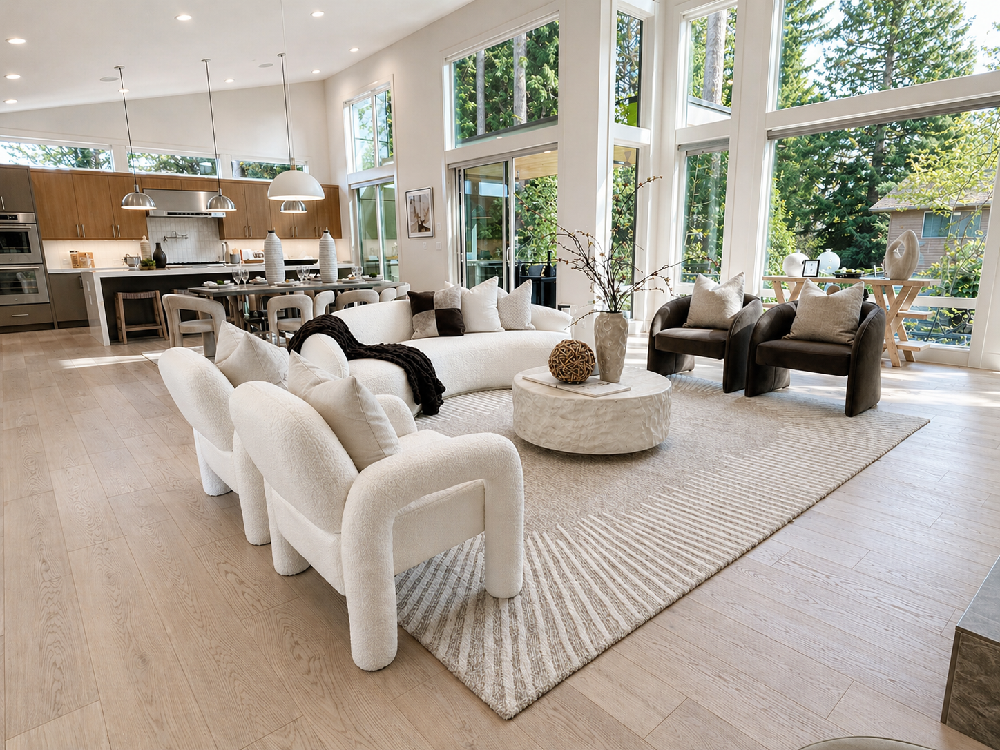 Bright modern living room with white sofas, a round coffee table, and large windows overlooking trees