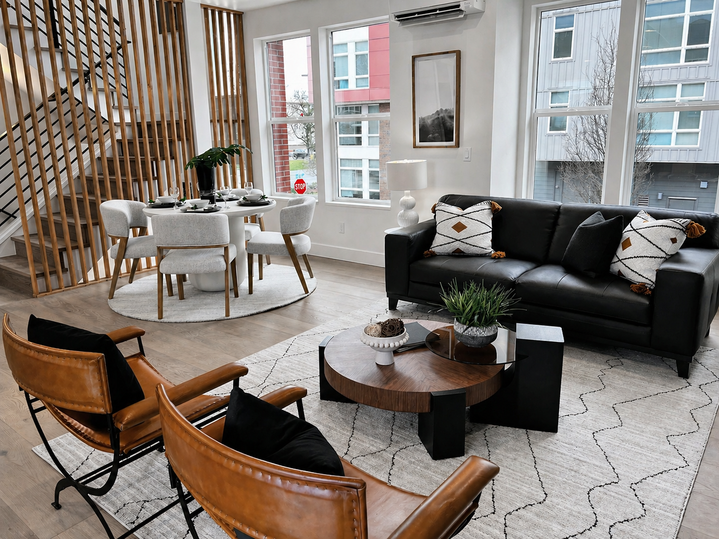 Modern living room with black sofa, tan chairs, round coffee table, and dining area by large windows