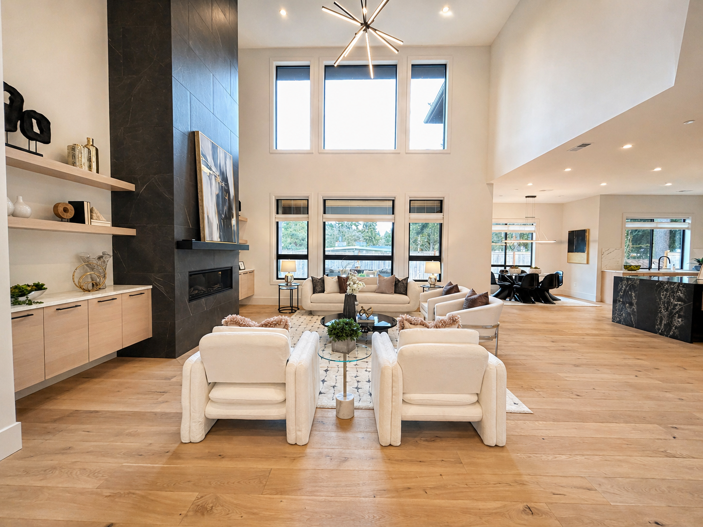 Bright modern living room with vaulted ceiling, white chairs, fireplace, large windows, and open kitchen.