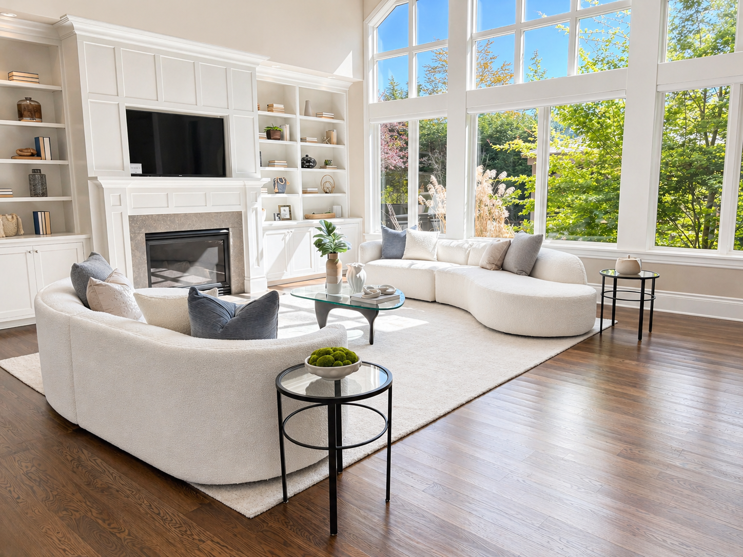 Bright modern living room with white sectional sofas, fireplace, large windows, and wood floors