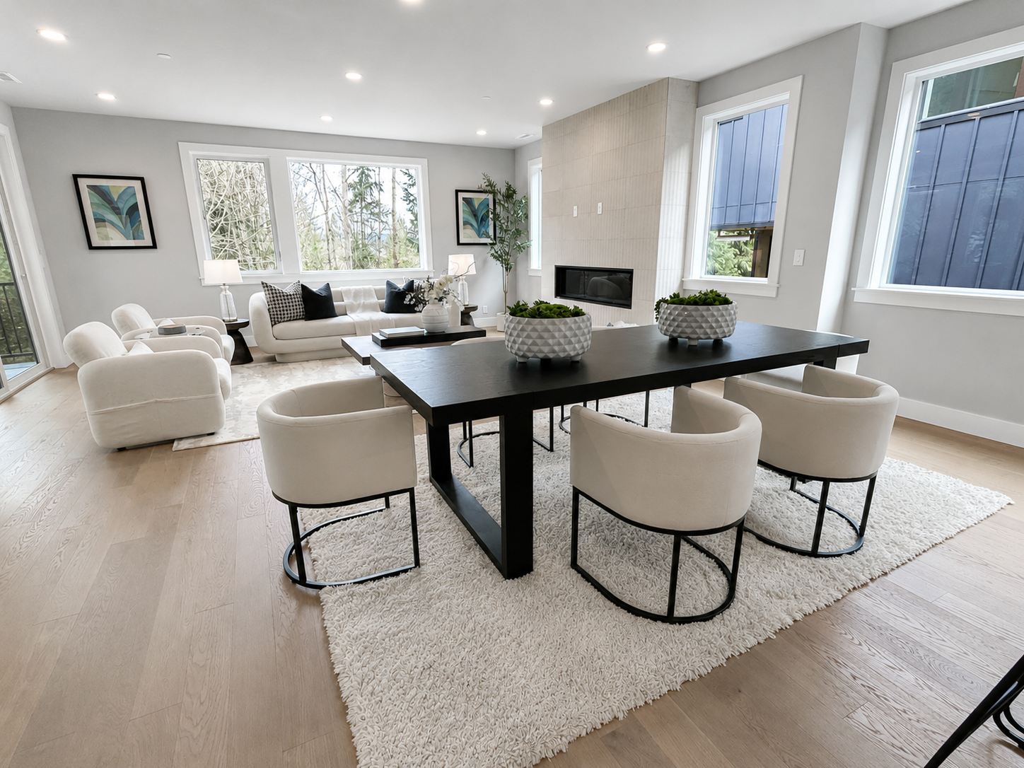 Bright modern living room with white sofas, black dining table, and large windows