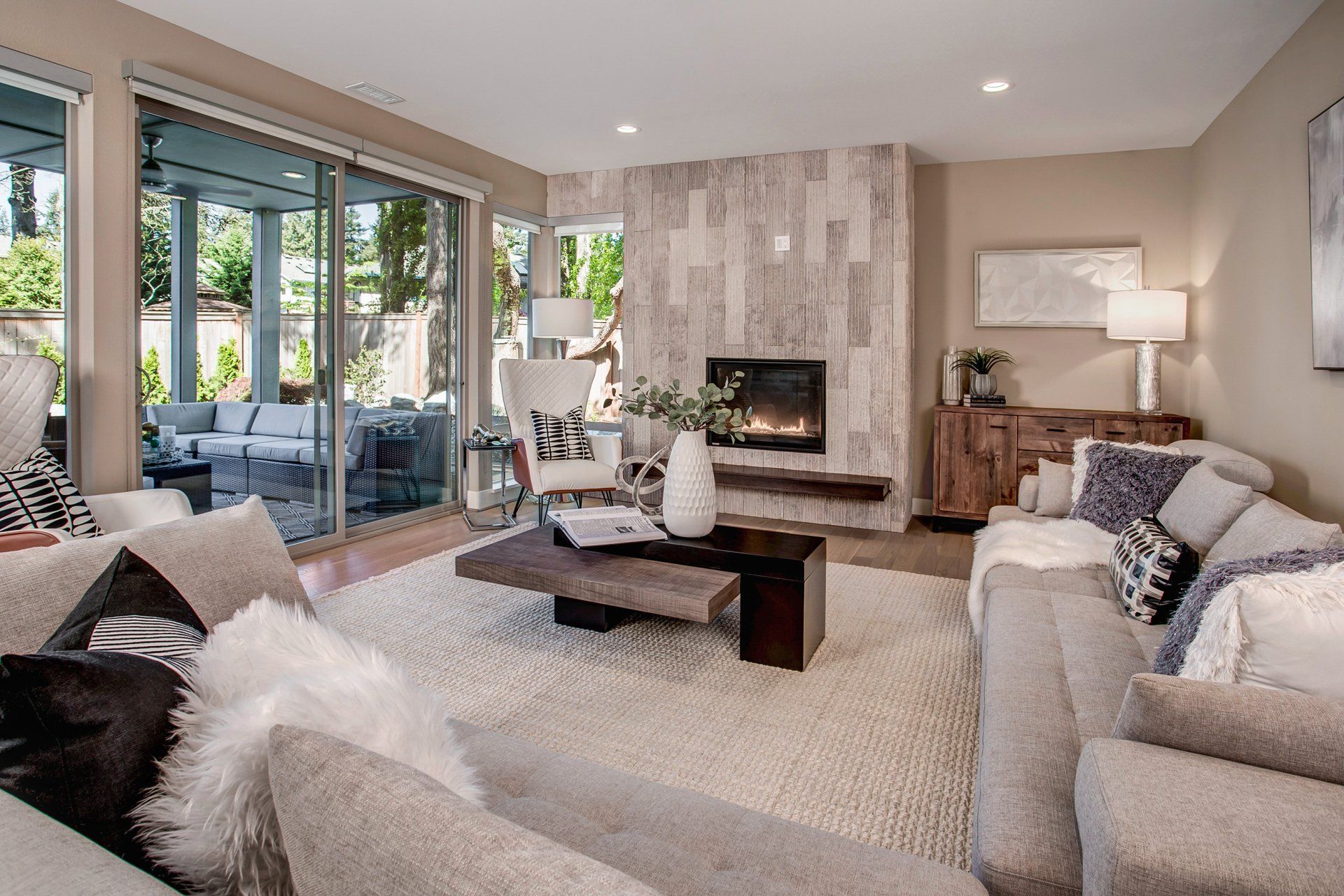 A modern living room with a fireplace, couches, and a sliding glass door to an outdoor patio.