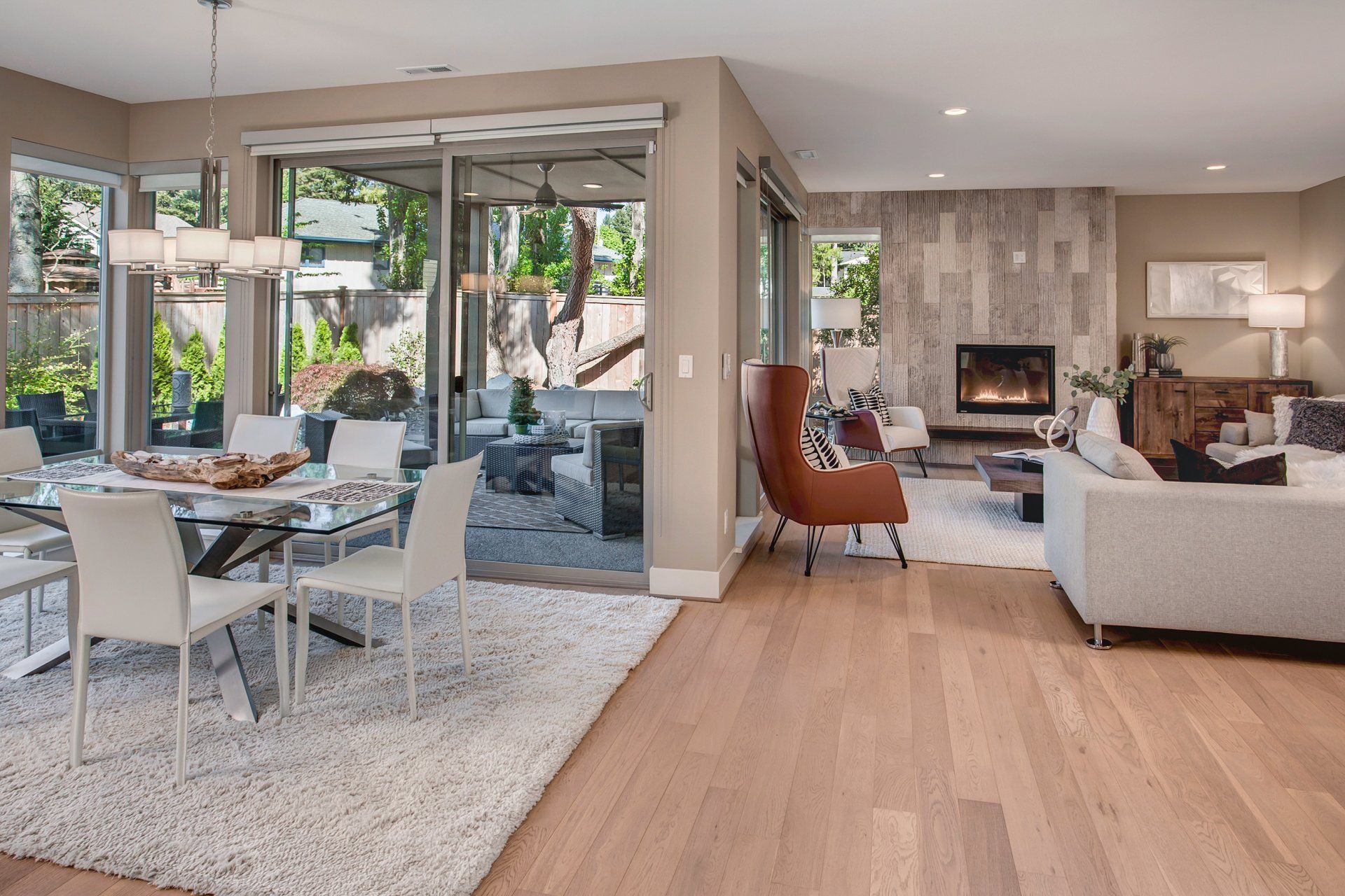 Open-concept living space with dining and living areas. Light wood floors, neutral walls, glass doors, and fireplace.