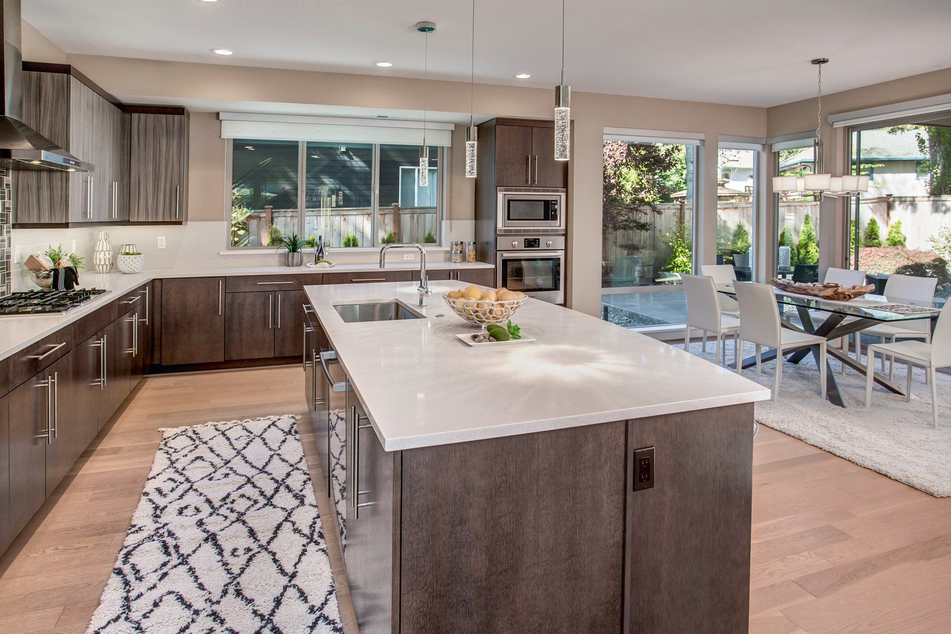 Modern kitchen with island, wood cabinets, and open dining area with large windows.
