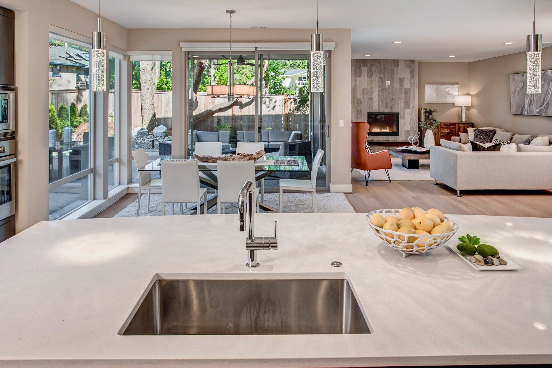Modern kitchen with island, sink, fruit bowl, open to dining and living areas, patio doors.