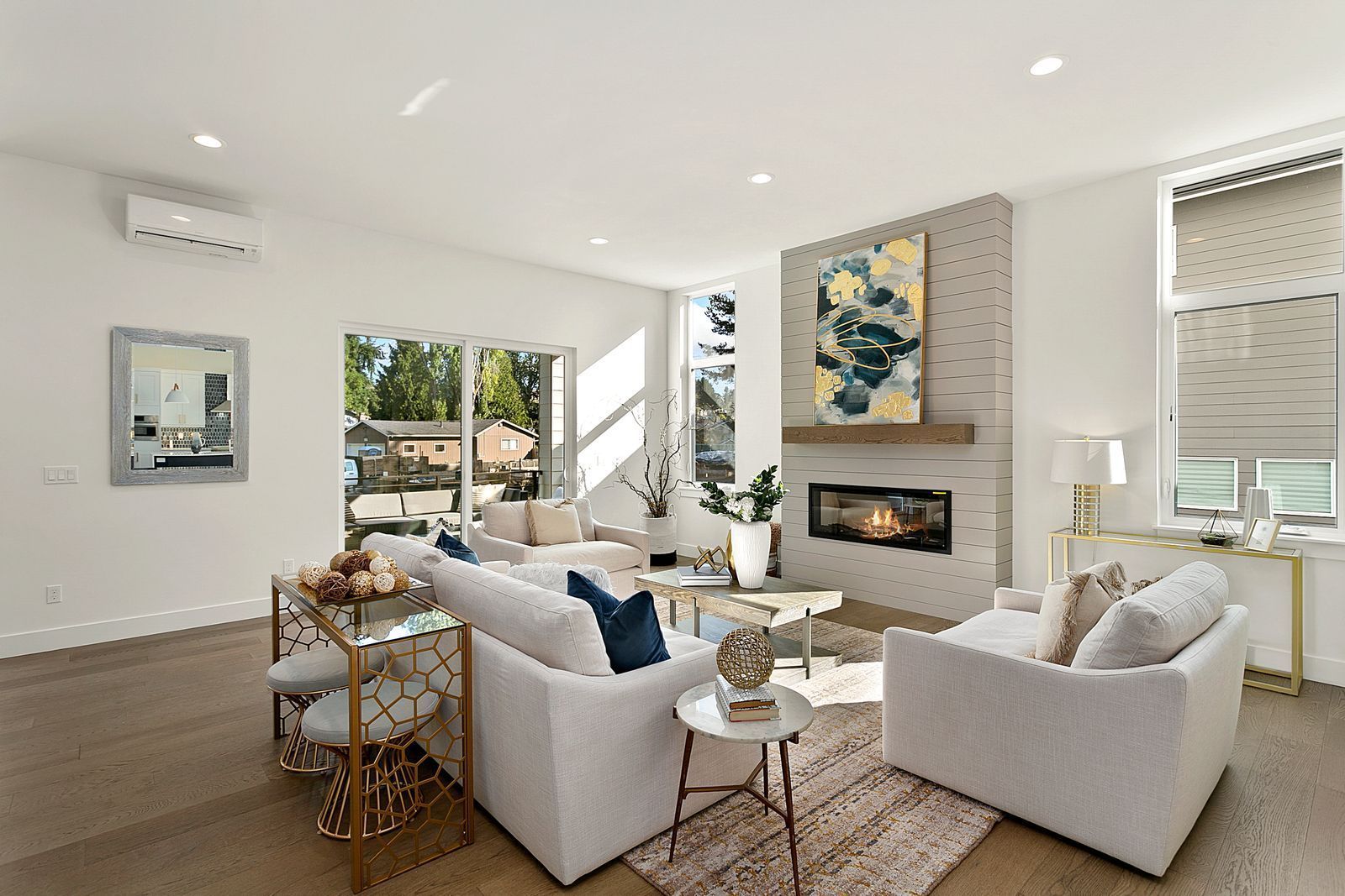 Bright, modern living room with white furniture, fireplace, and large windows; hardwood floors.