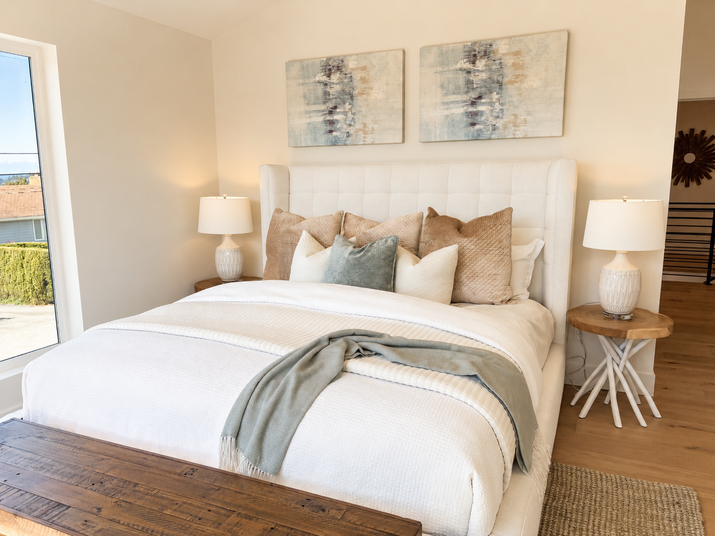 Bright neutral bedroom with a neatly made white bed, bedside lamps, and framed wall art
