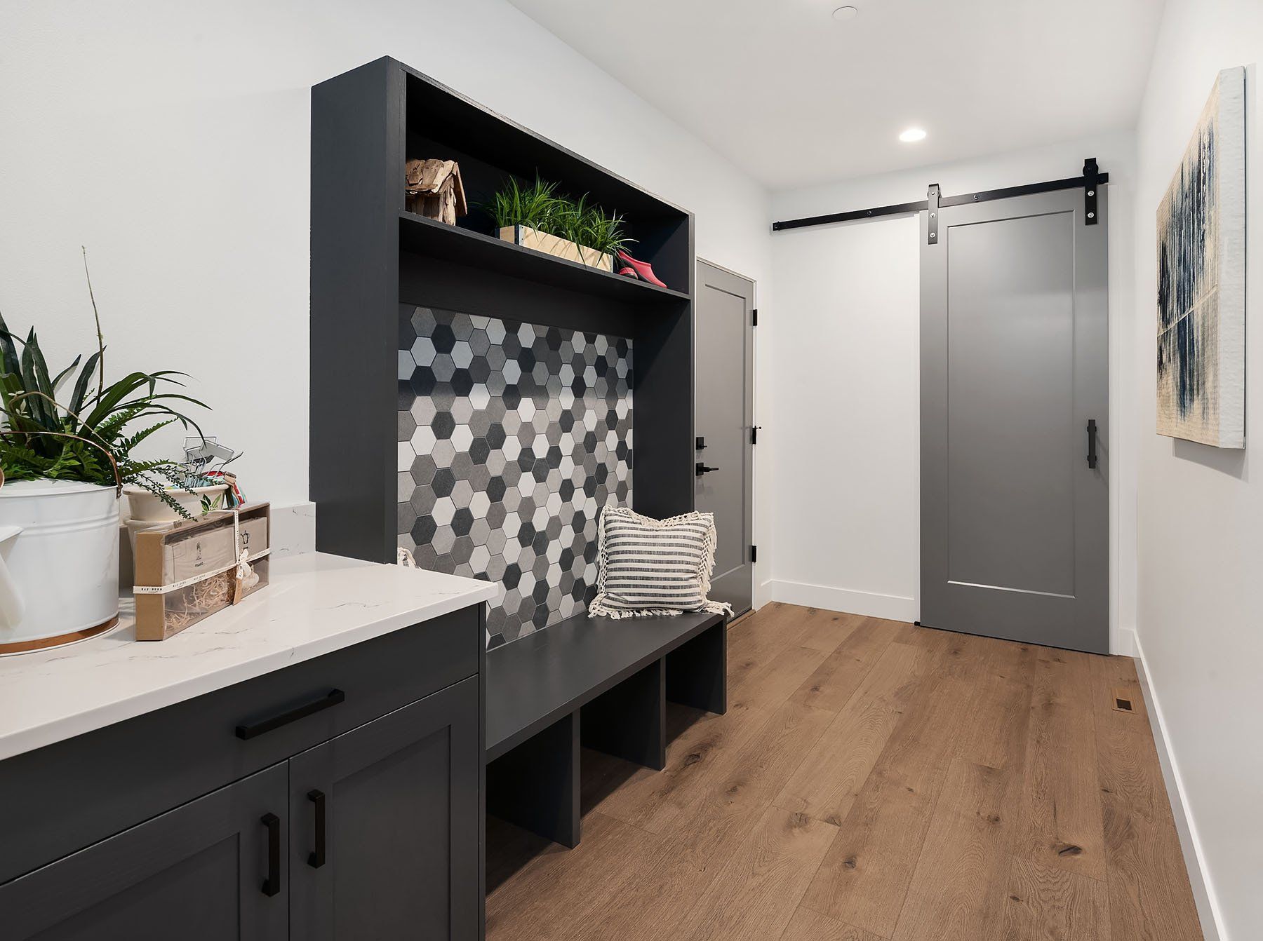 A gray mudroom with a bench, storage, and a sliding door on wooden floors.