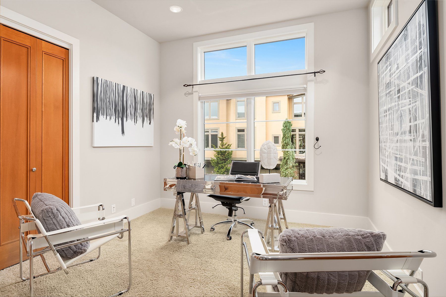 Office with a desk, two chairs, large window, art on walls, and a light-colored rug.