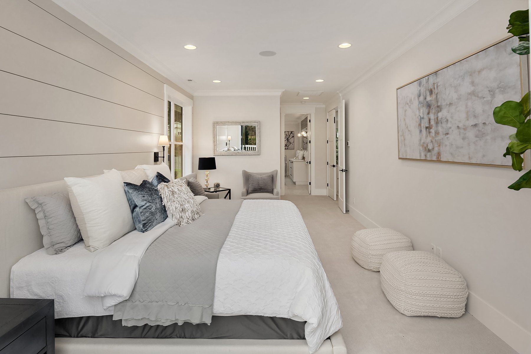 Bedroom with white bedding, gray accents, and wall art; two fluffy poufs sit on the floor.