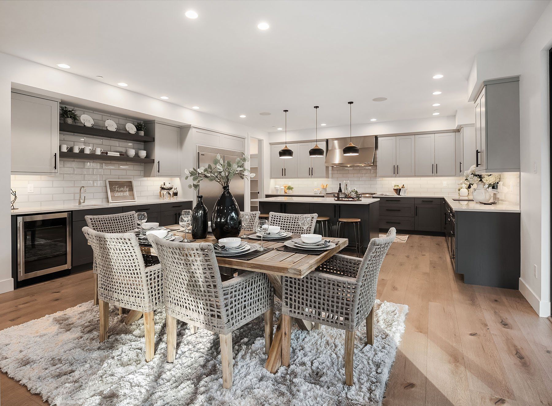 Modern kitchen and dining area with gray cabinets, wooden table, patterned chairs, and a fluffy rug.