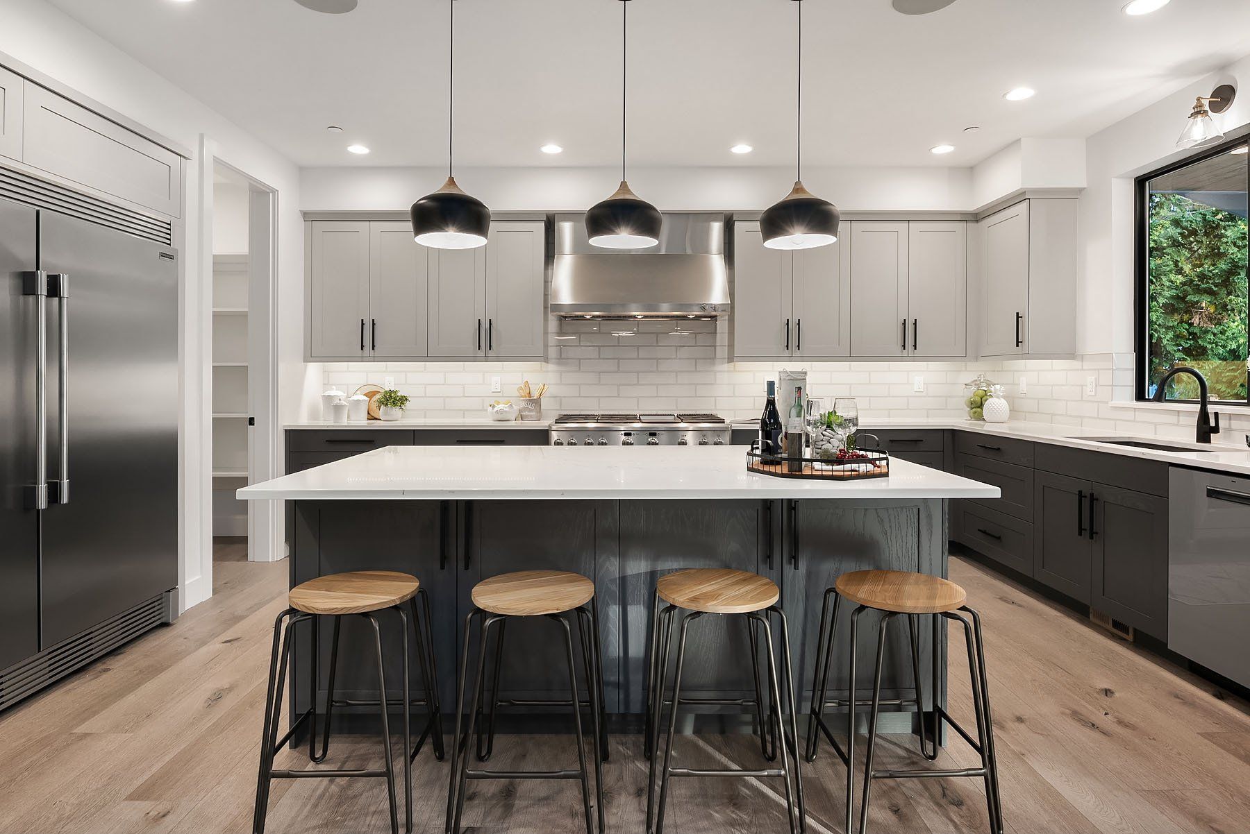 Modern kitchen with gray and black cabinets, a white island, and wooden stools.