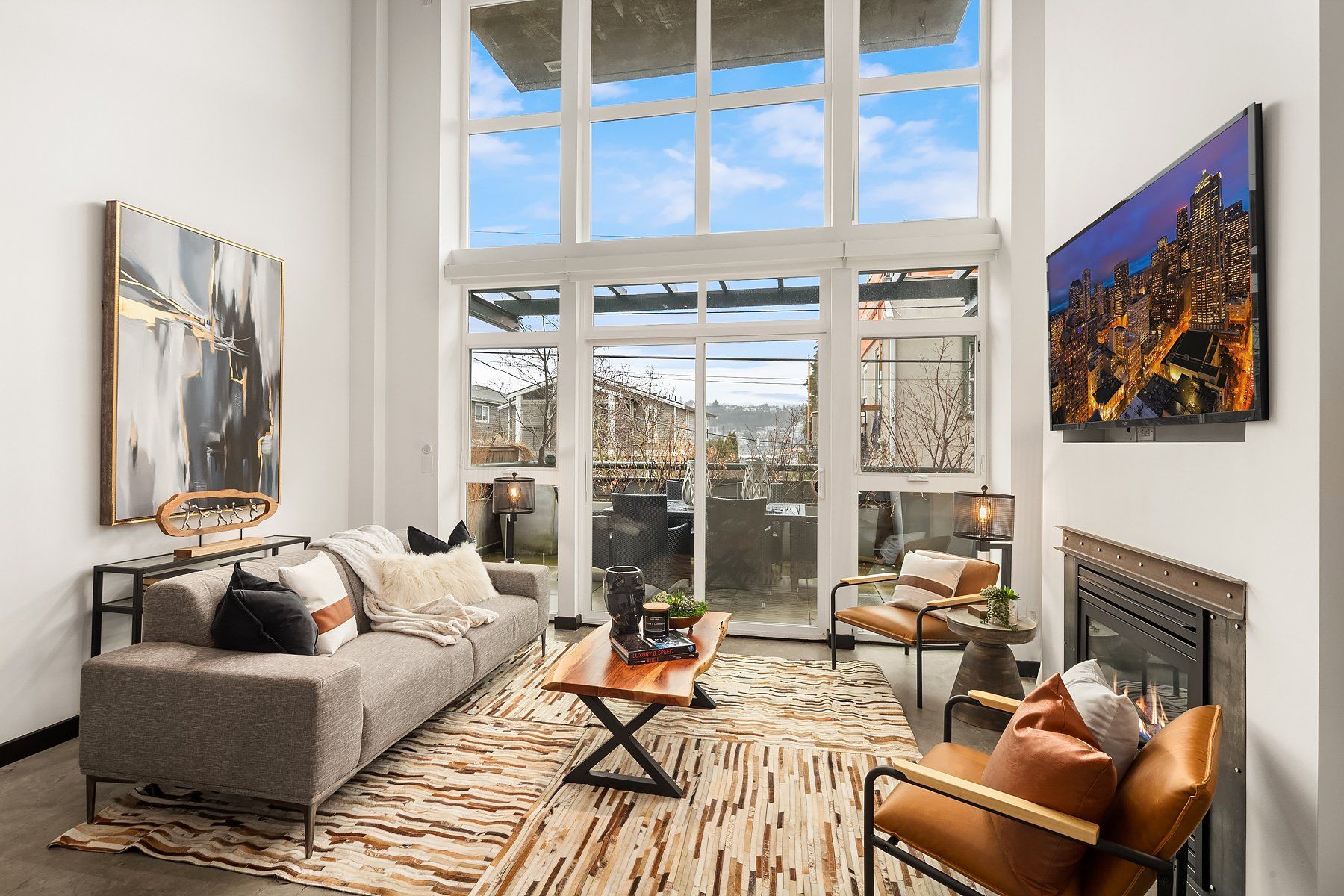 Living room with high windows, gray sofa, brown rug, fireplace, and city views.