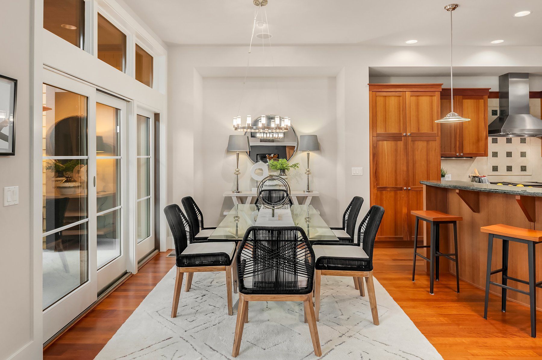 Dining room with table set for a meal; black chairs, wooden floor, and kitchen in the background.