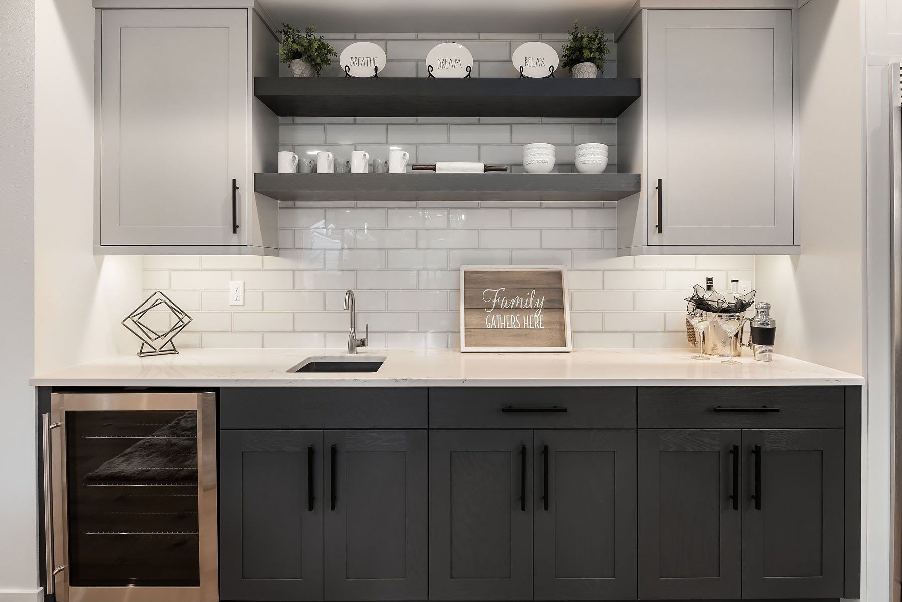 Modern home bar with cabinets, shelves, sink, and a wine fridge. Gray and white color scheme.