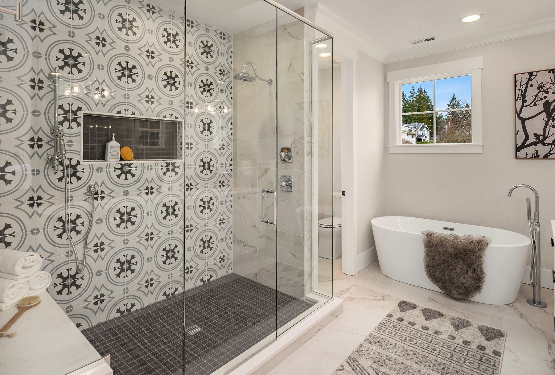 Bathroom with patterned tile shower, glass enclosure, freestanding tub, and window.
