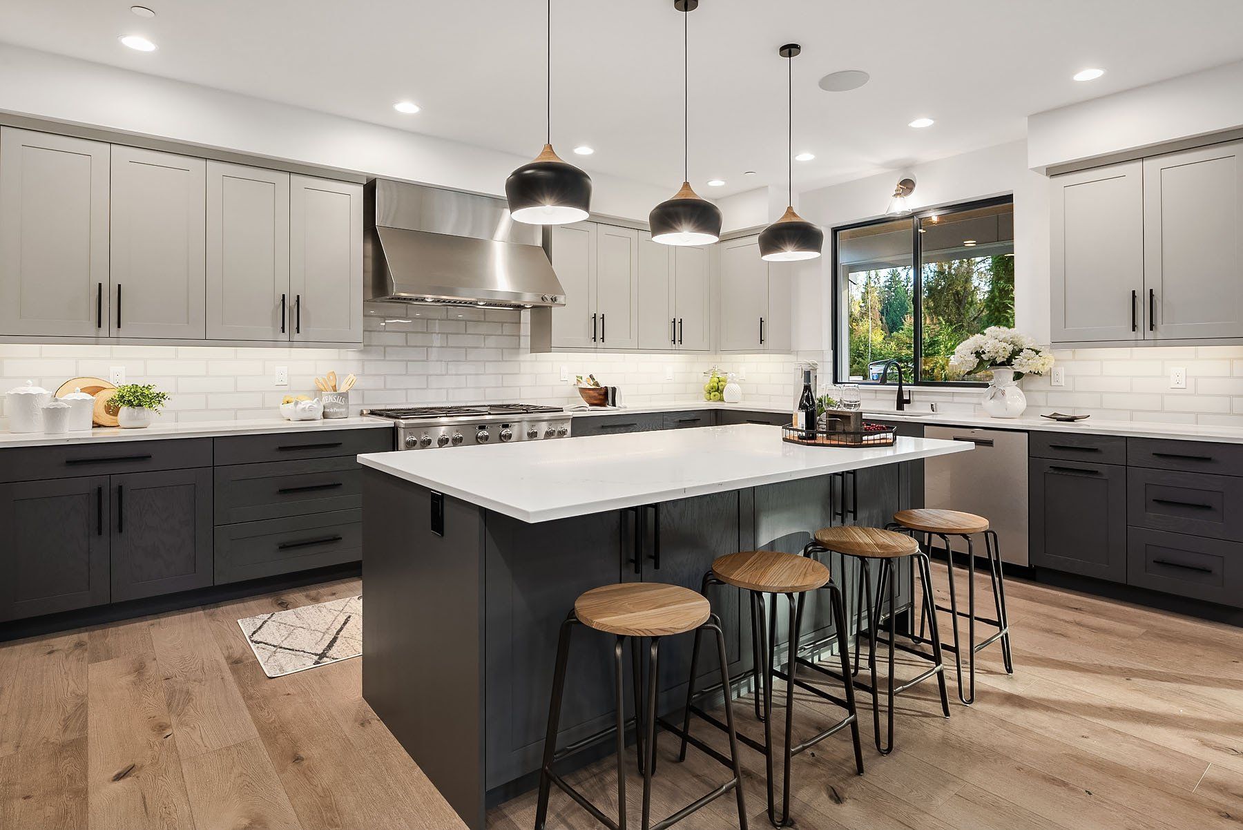 Modern kitchen with gray and white cabinets, island with stools, and large window.