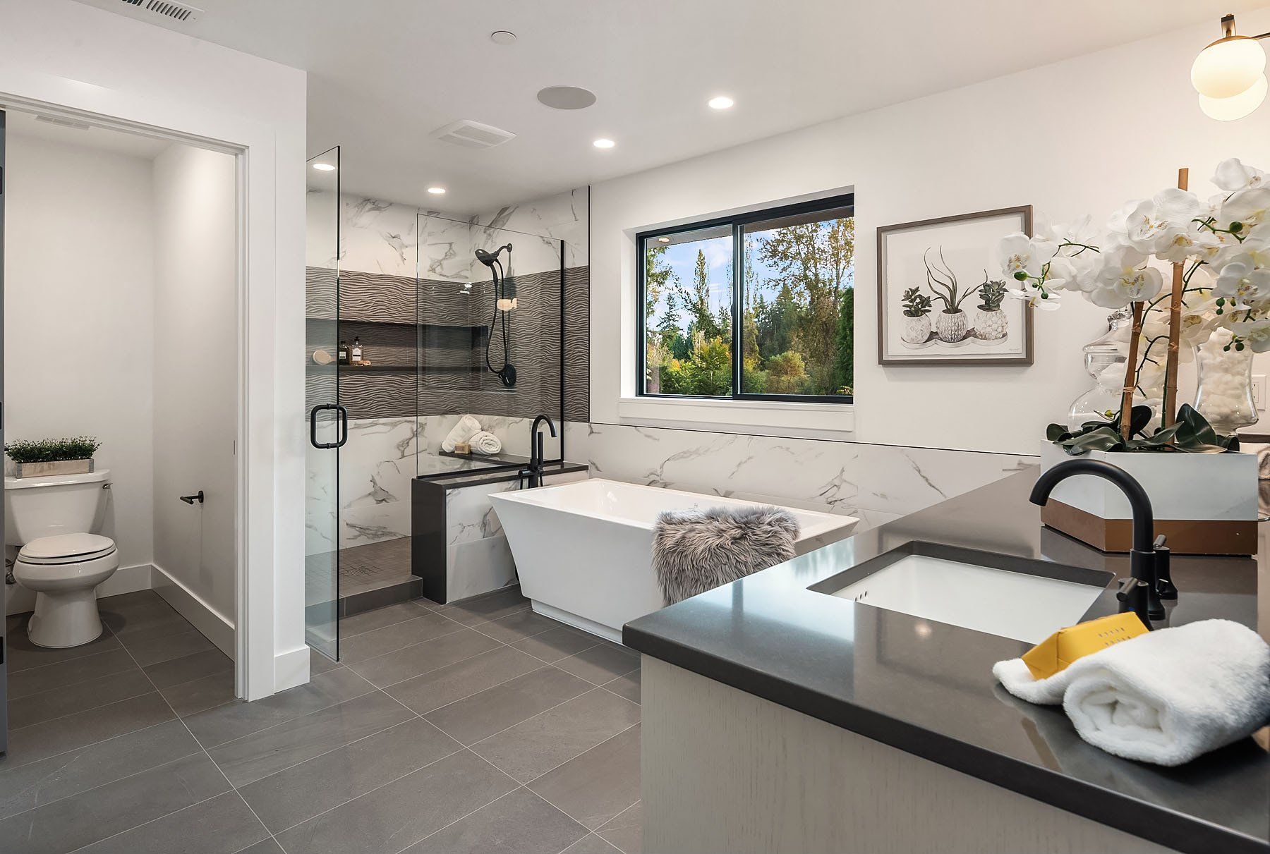 Modern bathroom with white tub, dark countertop, and window overlooking trees.