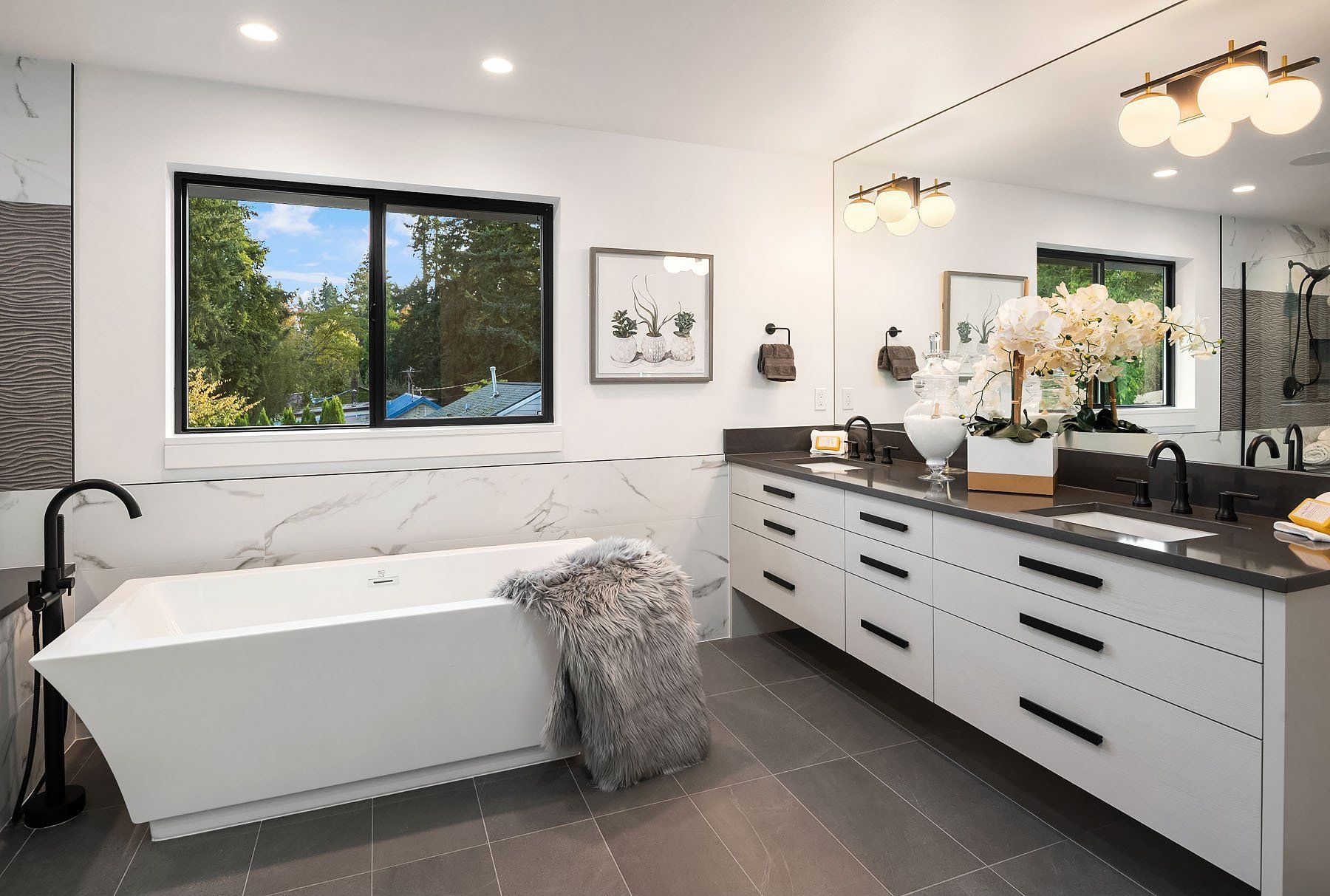 Modern white bathroom with a soaking tub, vanity, large window, and black fixtures.