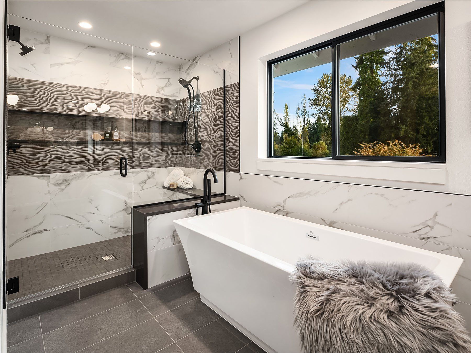 Modern bathroom with a freestanding tub, shower, and large window overlooking trees.