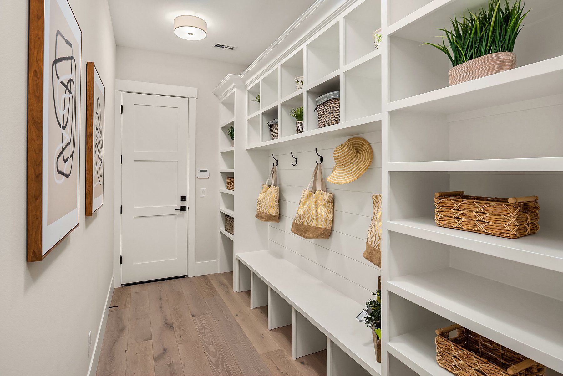 A bright, white hallway with built-in shelves, a bench, and coat hooks. Two framed prints hang on the left wall.