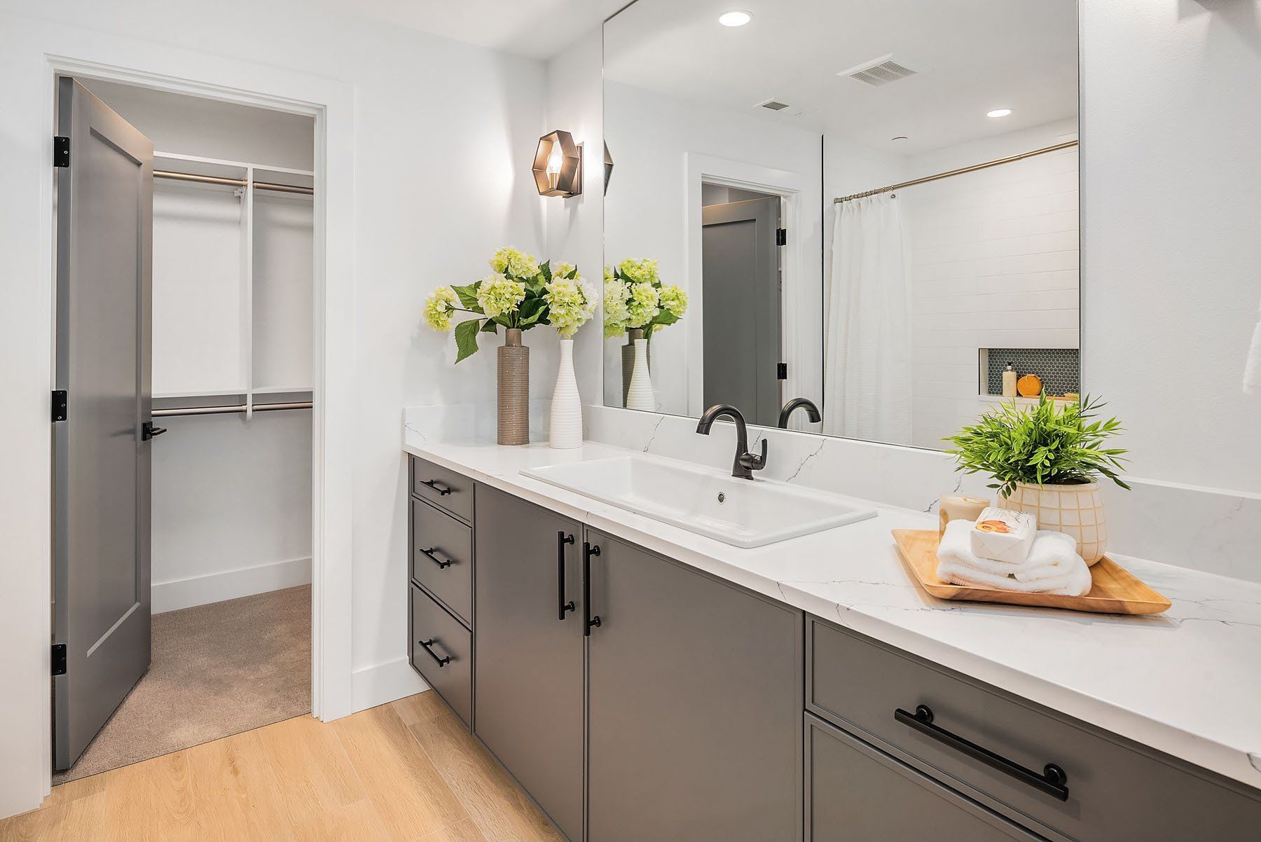 Bathroom with gray cabinets, white countertop, large mirror, and open closet.