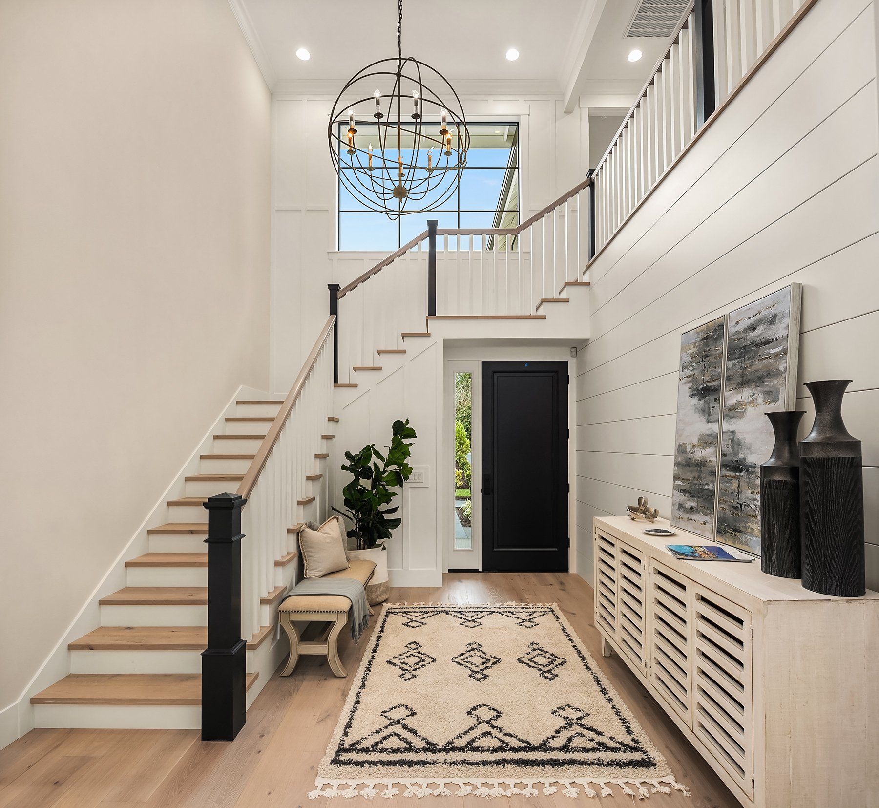 Entryway with stairs, a black door, a white console, and a patterned rug.